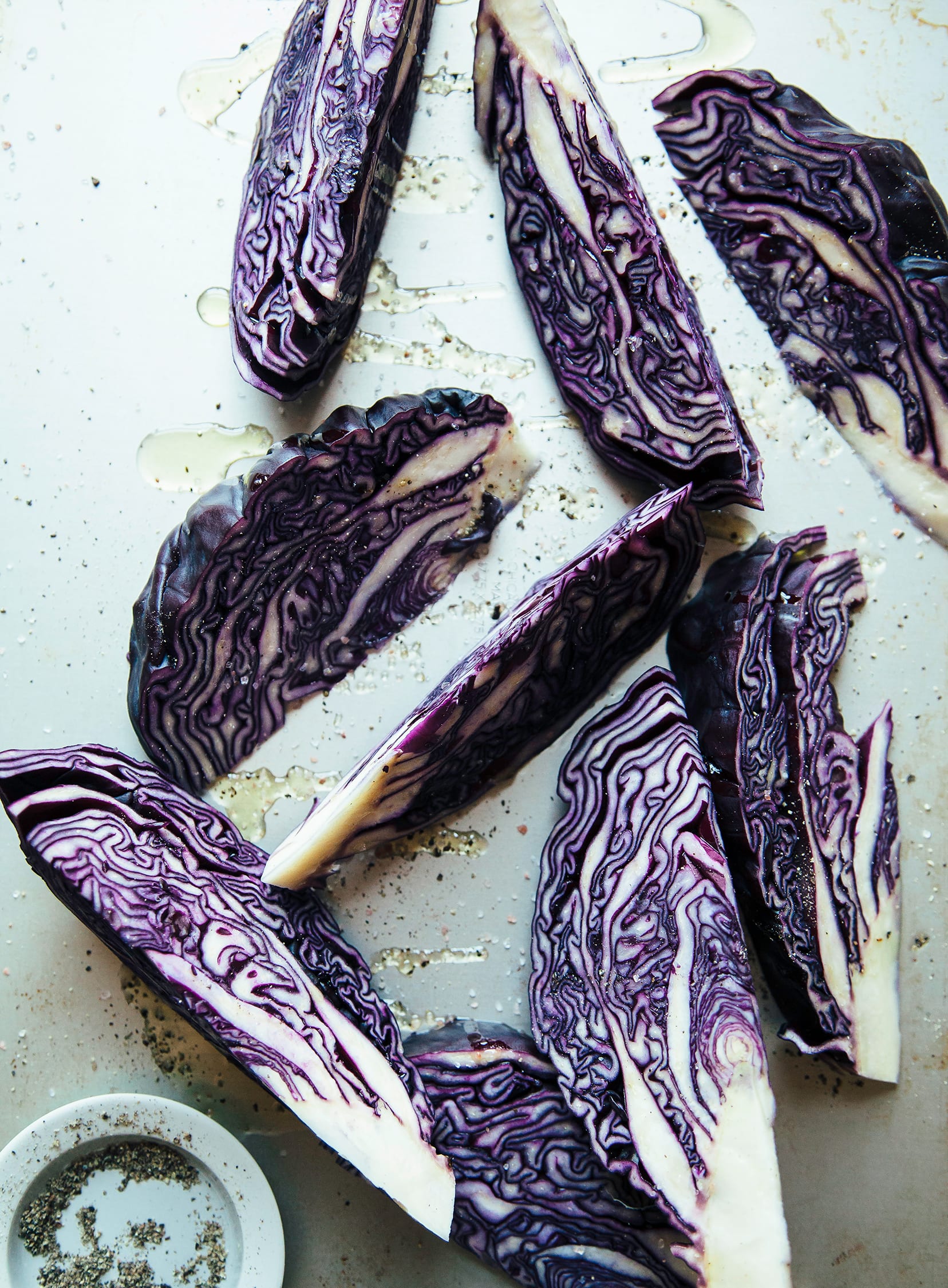 Overhead shot of purple cabbage wedges coated in oil and sprinkled with salt and pepper.