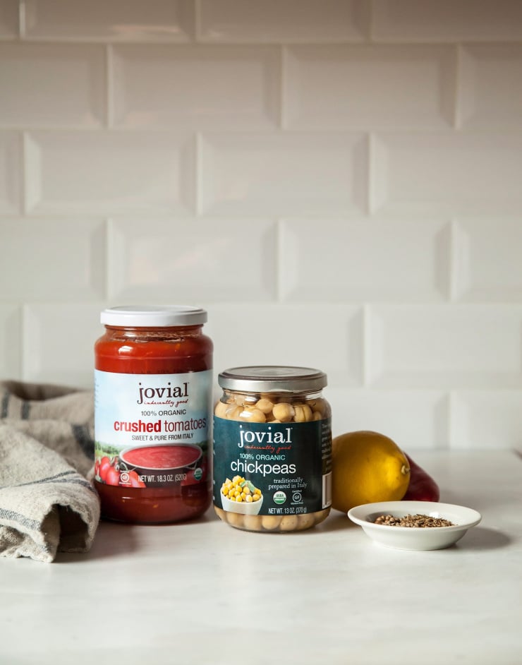 A head-on shot shows ingredients on the counter: crushed tomatoes, chickpeas, lemon, and a small bowl of spices.