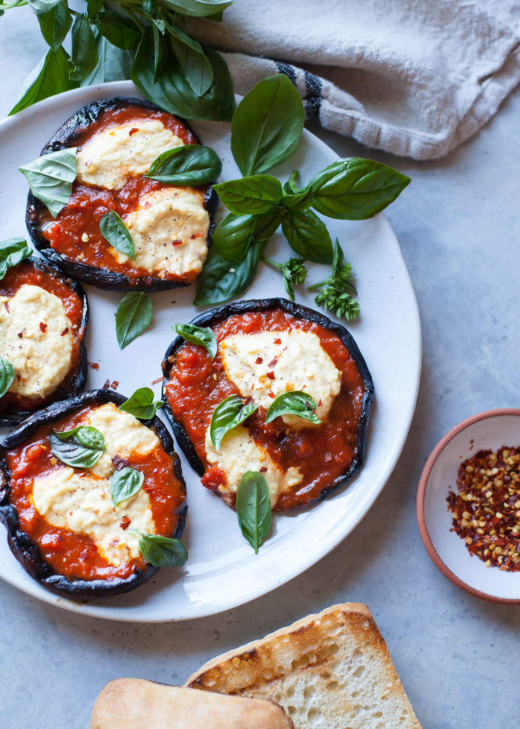 An overhead shot of grilled pizza portobellos with dollops of creamy vegan cashew “ricotta” and basil leaves on top.