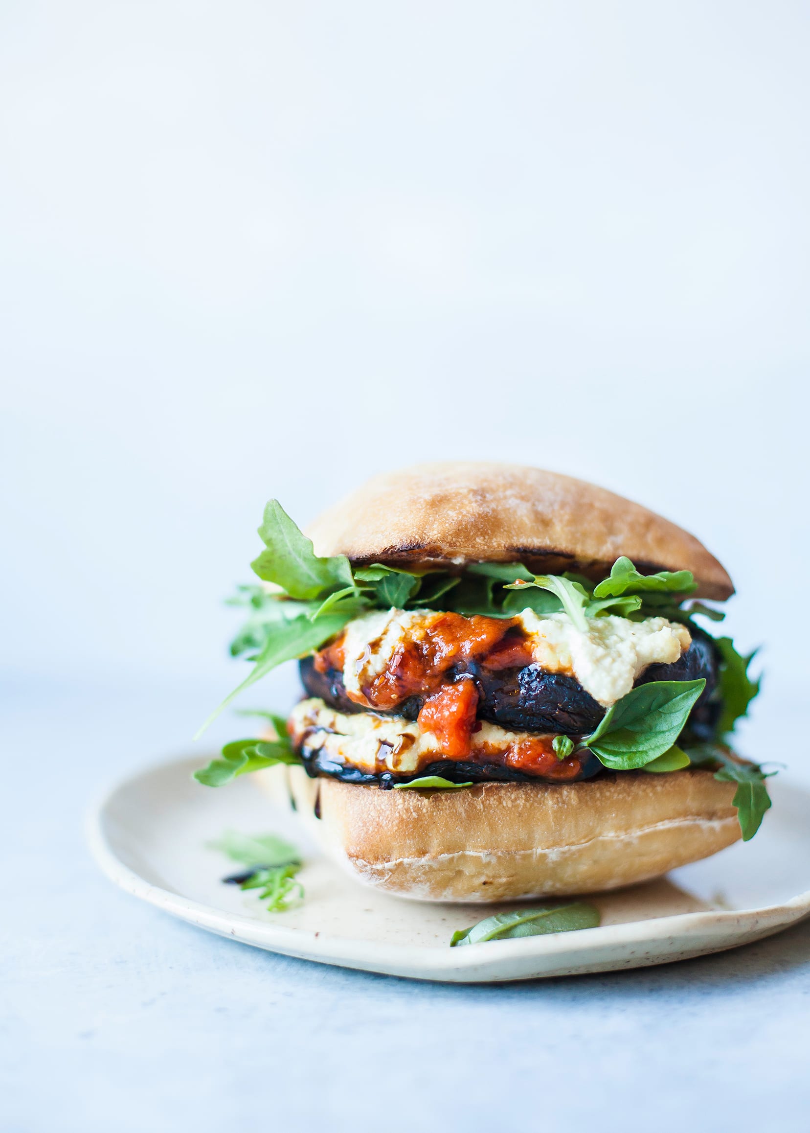 Image shows a very messy portobello pizza burger sandwich with fresh arugula and basil leaves sticking out.