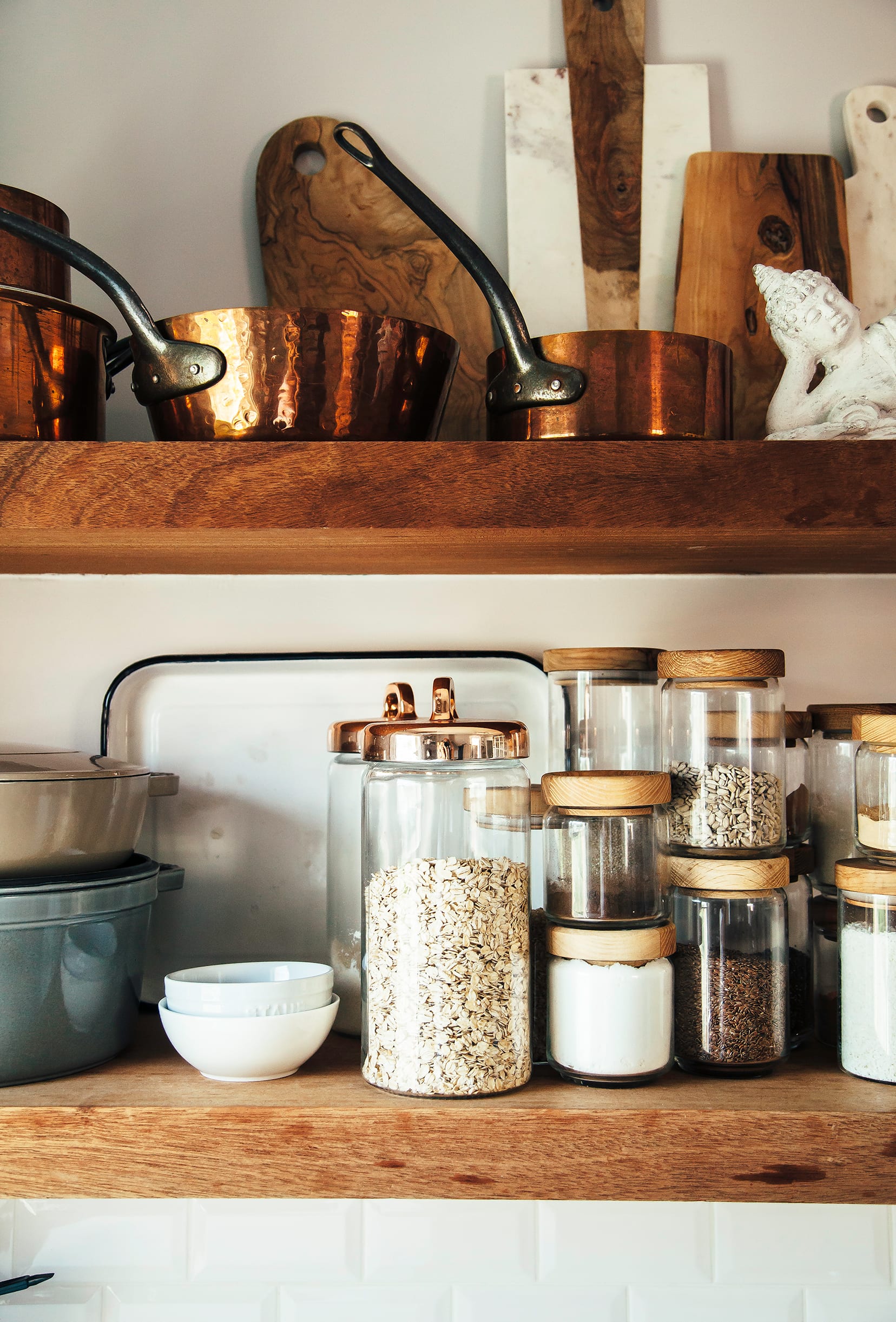 Image shows open kitchen shelves with jars of grains, seeds and spices, as well as copper pots.