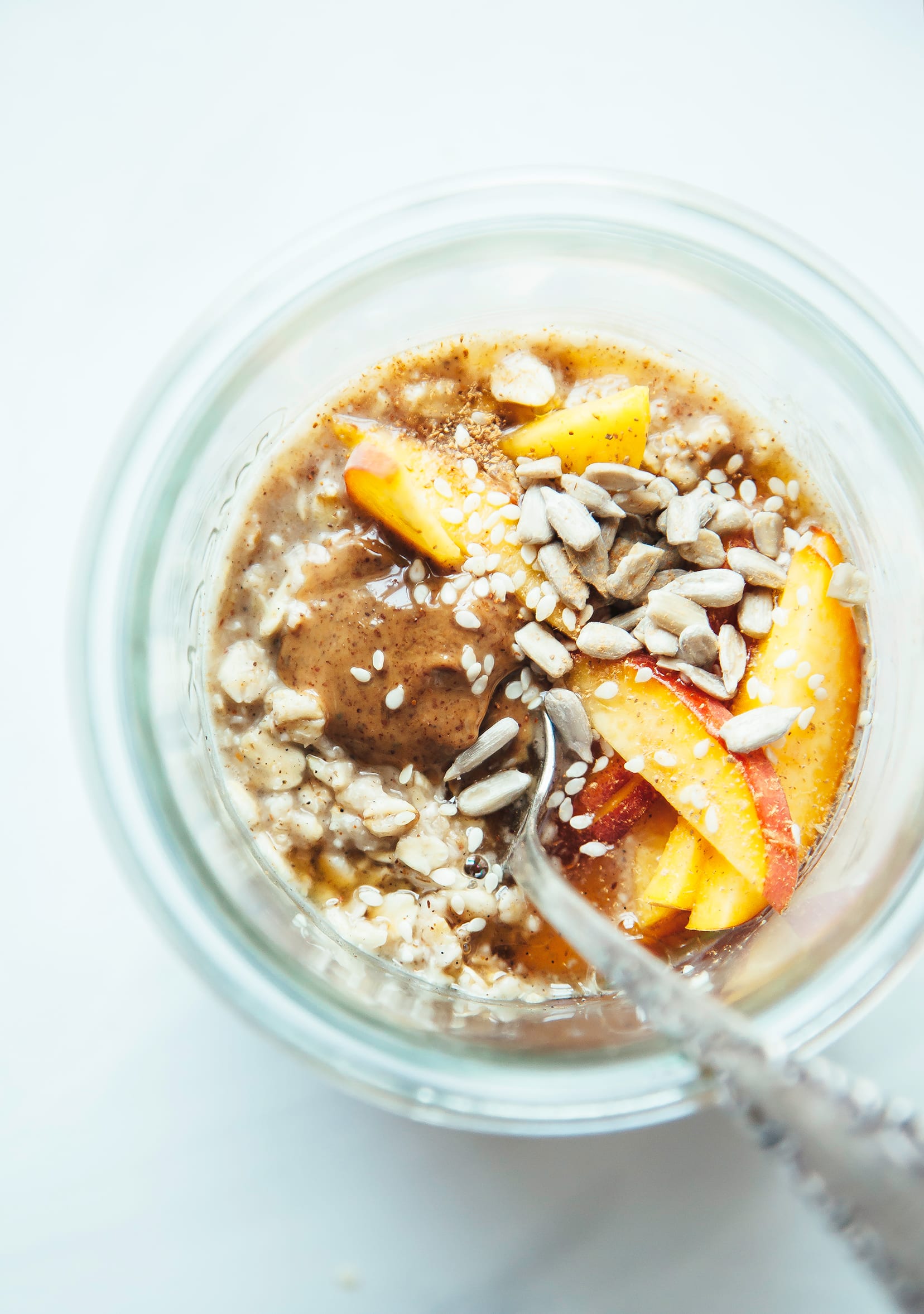 An overhead shot of oatmeal in a glass jar, topped with sliced peaches and sunflower seeds.
