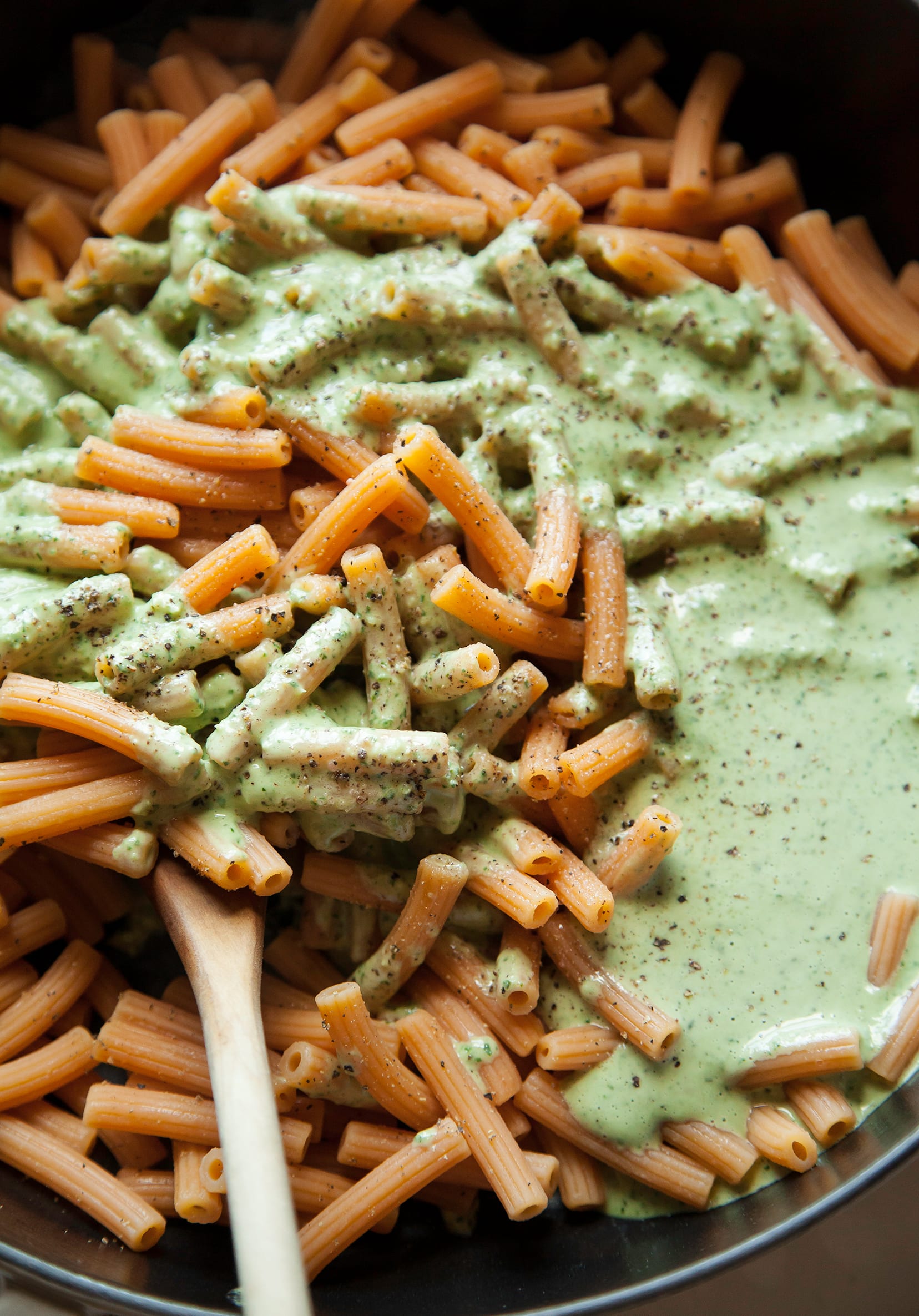 Image shows a light green cream being added to cooked lentil pasta.