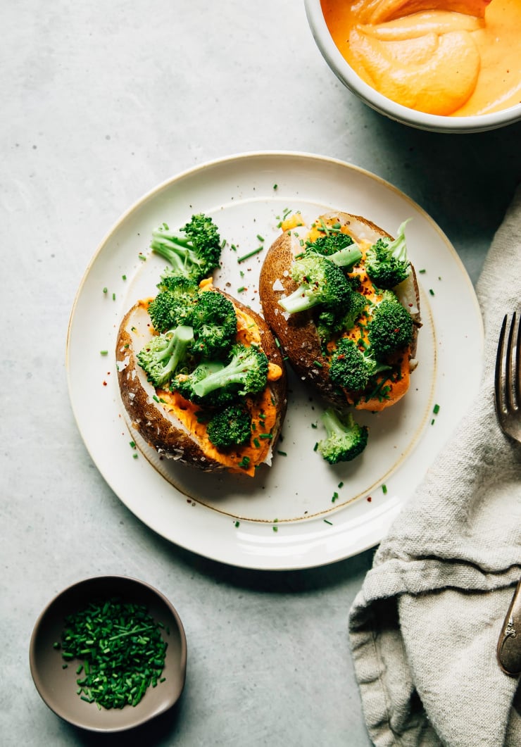 An overhead shot of two baked potatoes filled with a creamy orange sauce and chopped steamed broccoli.