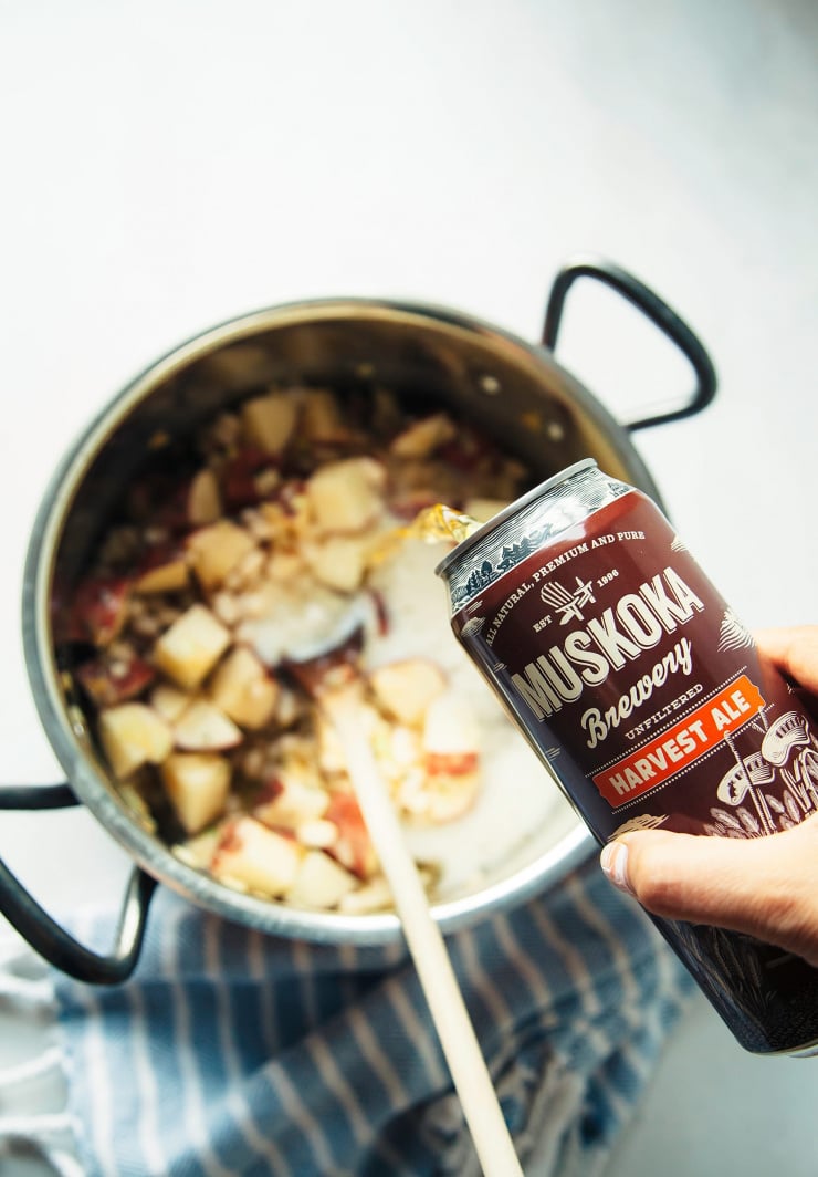 A hand pouring some beer into a pot of soup.