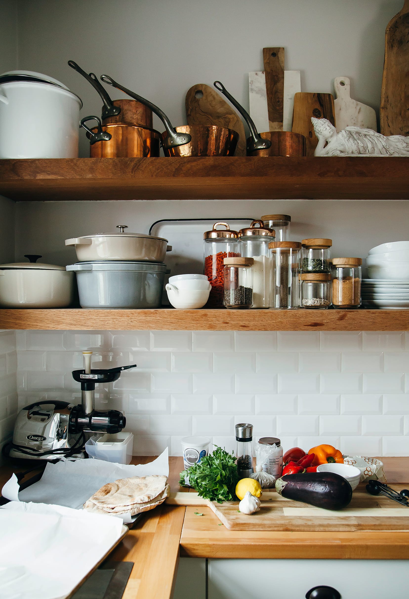 Image shows a kitchen scene with vegetables, herbs, and pita on the counter.