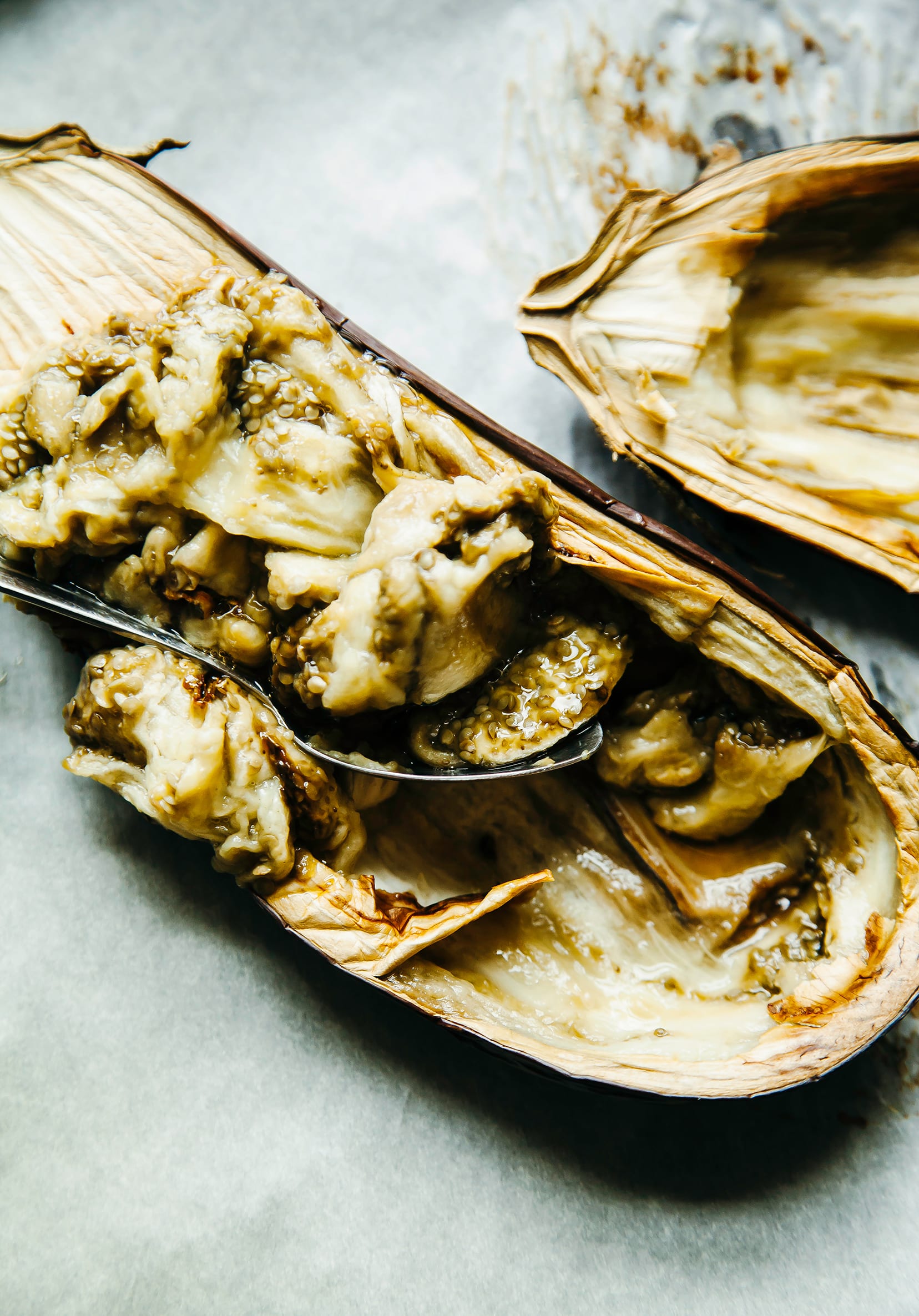 Image shows roasted eggplant halves being scooped out by a spoon.