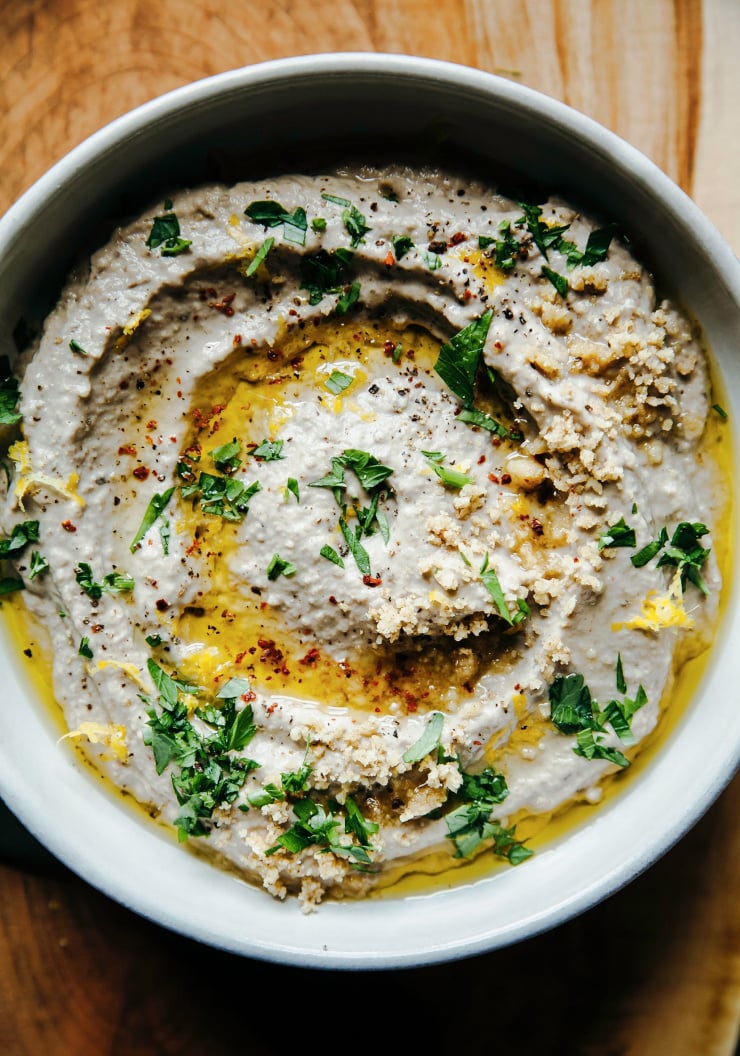 An up close, overhead shot of a creamy beige eggplant dip topped with olive oil, lemon zest and chopped parsley.