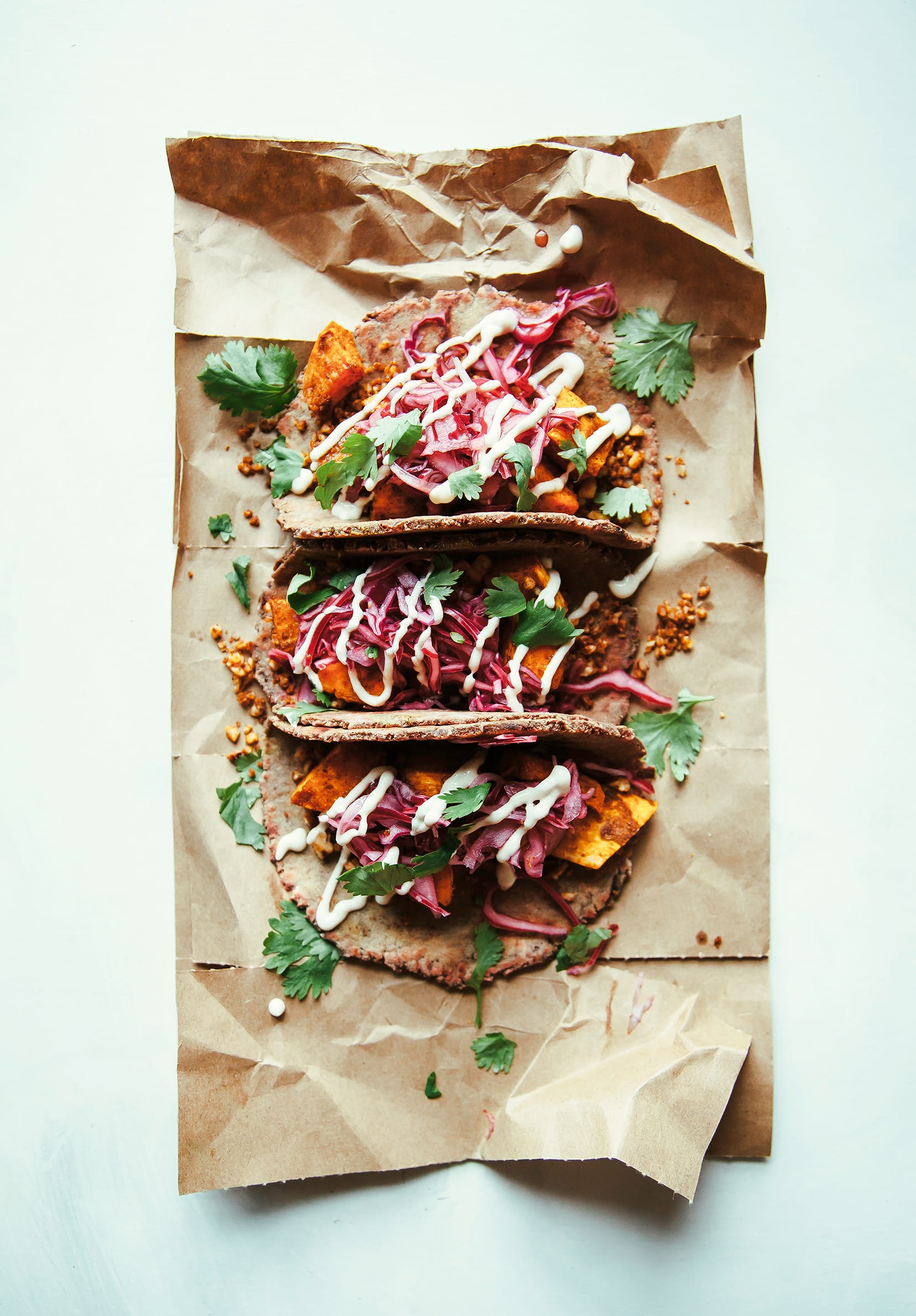 An overhead shot of 3 sweet potato tacos drizzled with a creamy white sauce and topped with chopped cilantro.