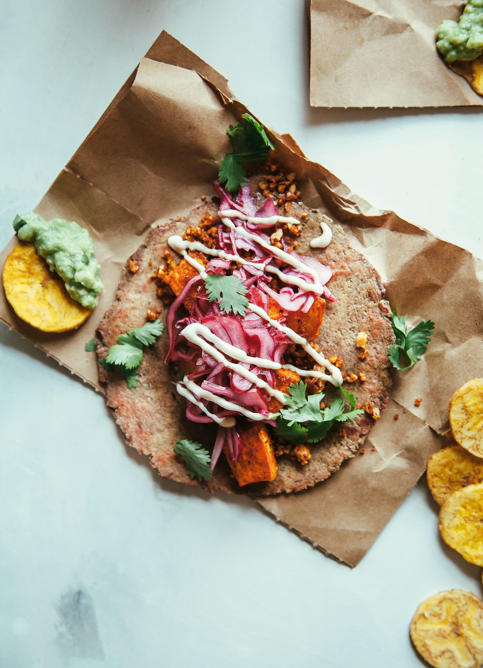 An overhead shot of a sweet potato pecan taco drizzled with a creamy white sauce and topped with chopped cilantro.