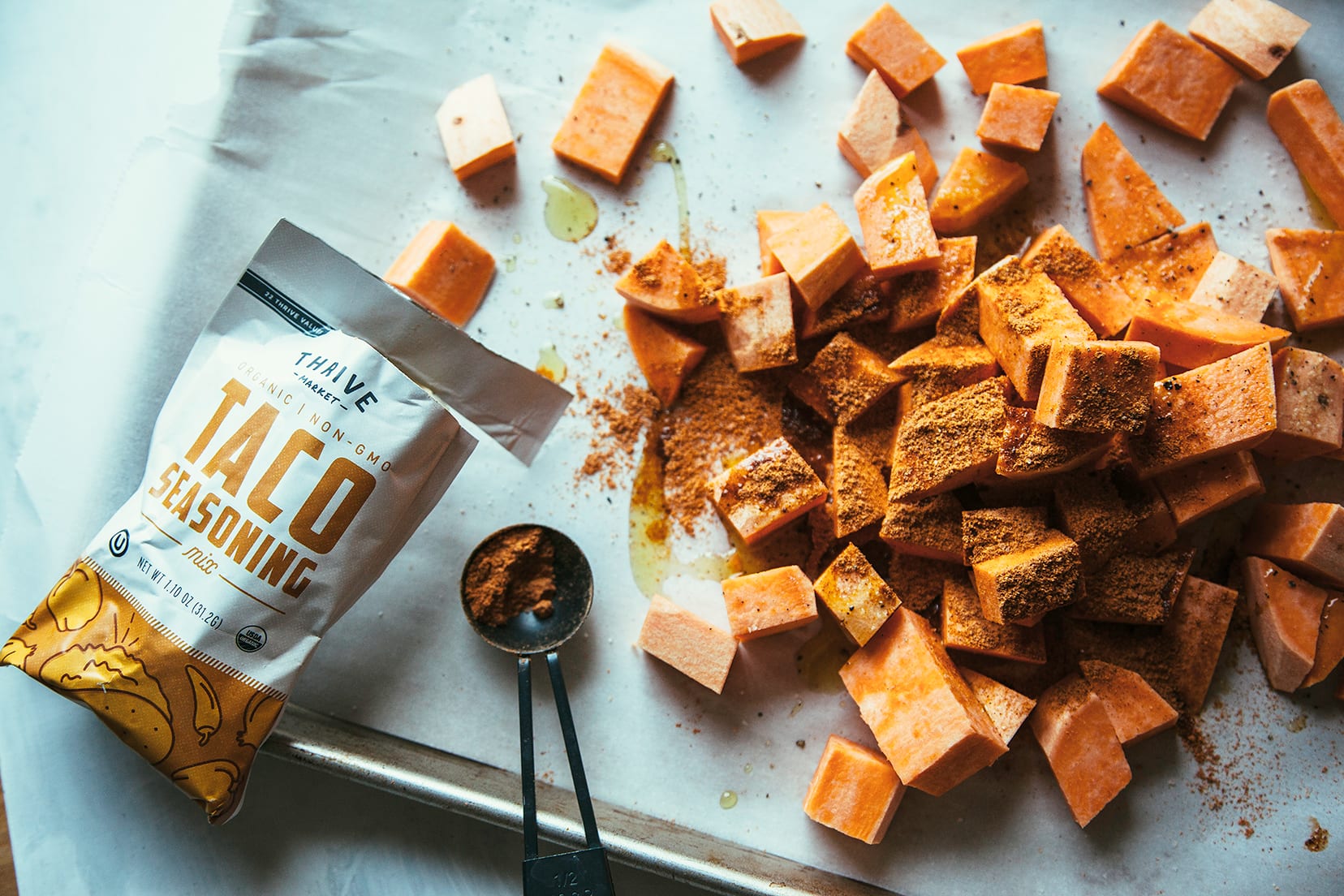 Image shows cubed sweet potatoes about to be tossed in taco seasoning on a baking tray.