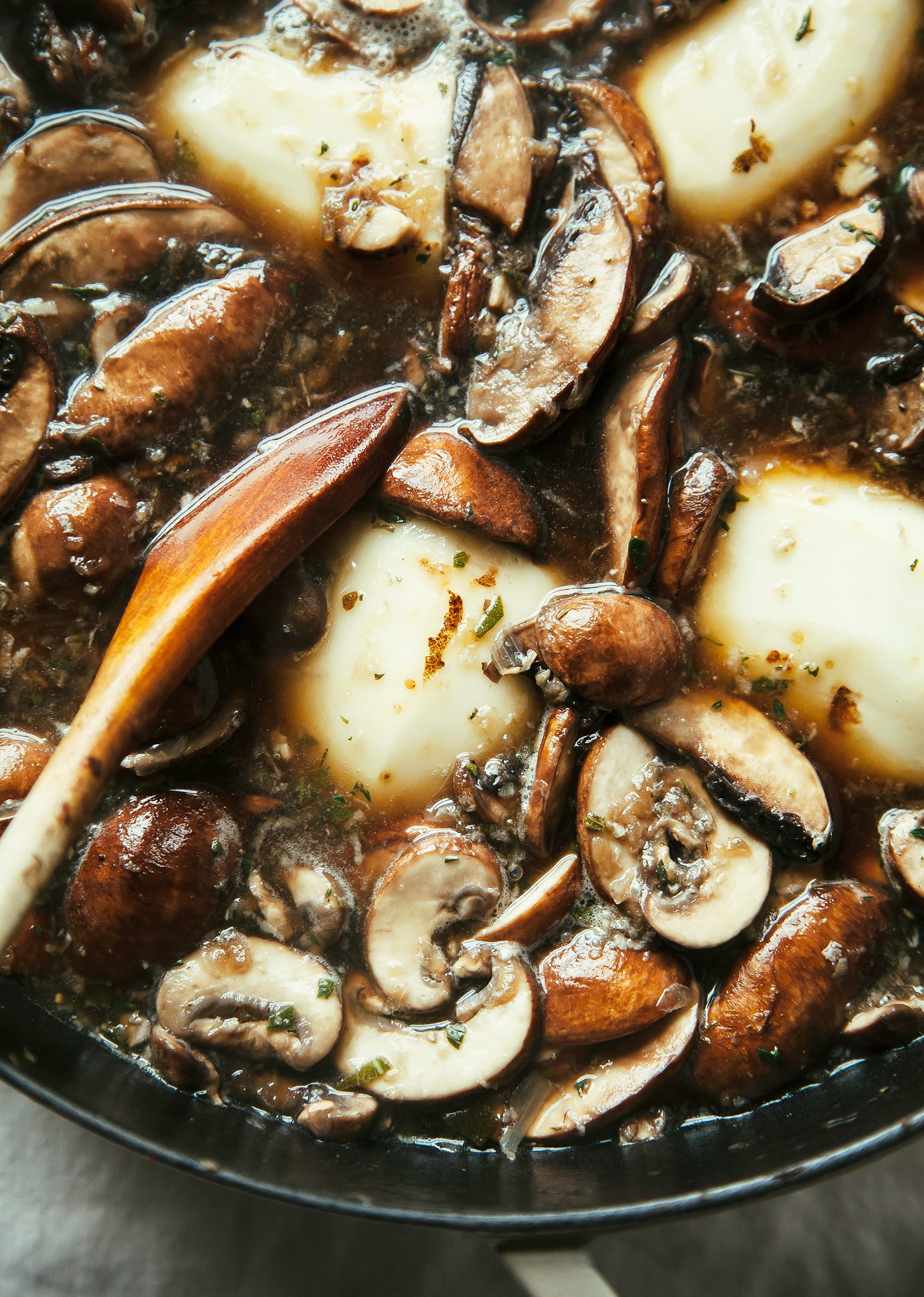 Image shows mushrooms and potatoes simmering in a pot, surrounded by liquid.