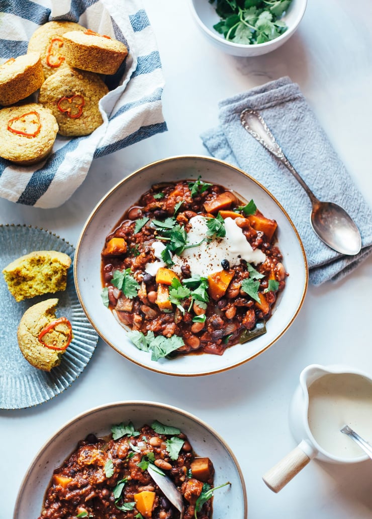 An overhead shot of a deep red squash chili with beans and quinoa. The chili is garnished with a vegan sour cream and cilantro.