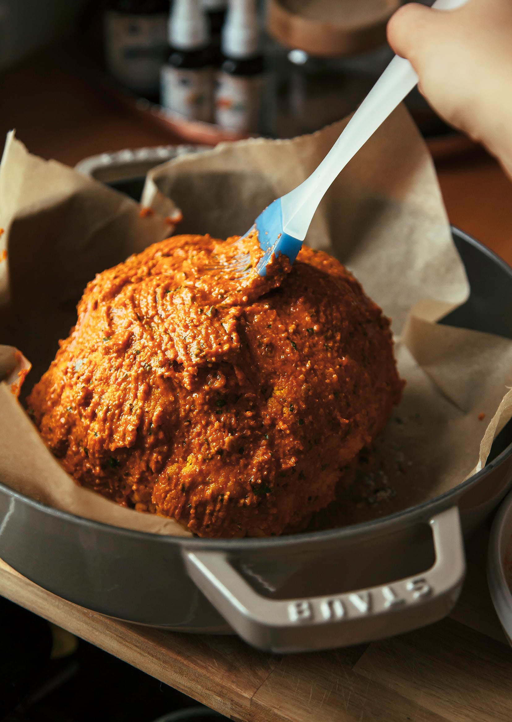 Image shows a hand brushing romesco onto the surface of a whole cauliflower.