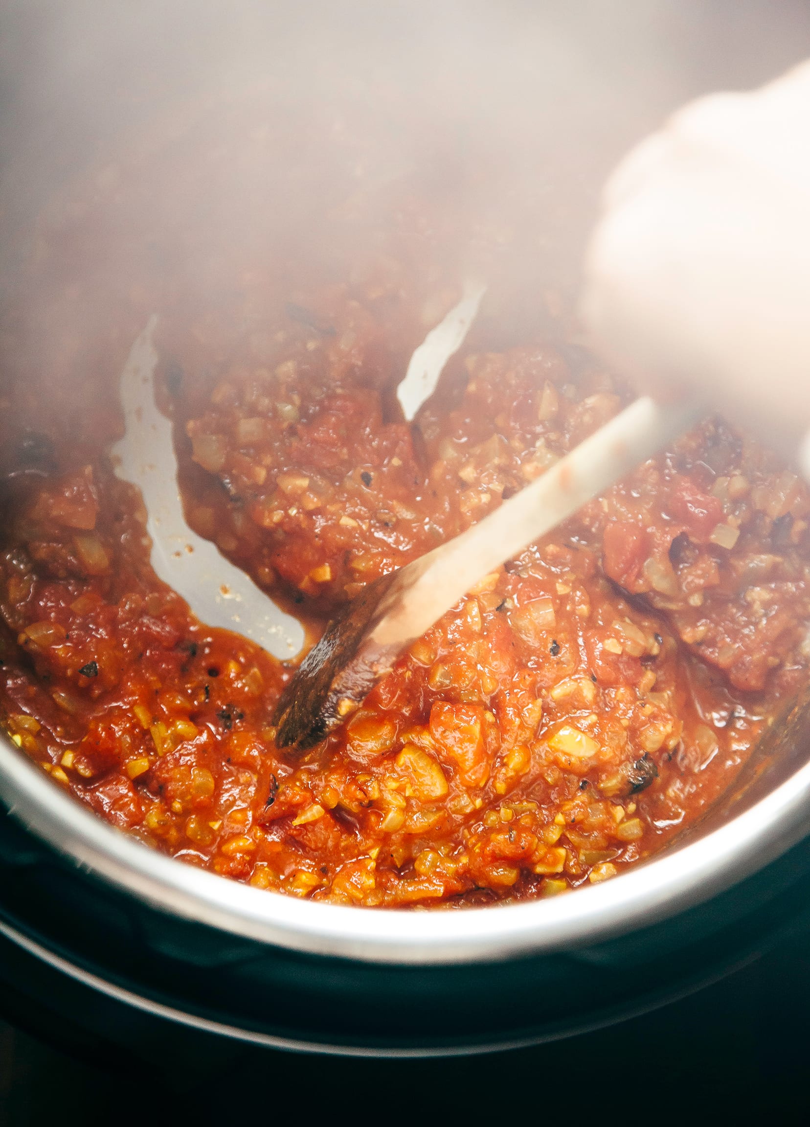 Image shows tomatoes, onions, and seasoning stewing in an Instant Pot with steam rising up.
