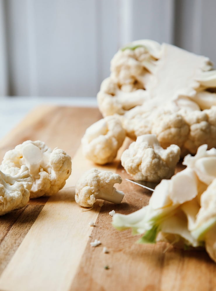 A head on shot of cauliflower being cut on a cutting board.