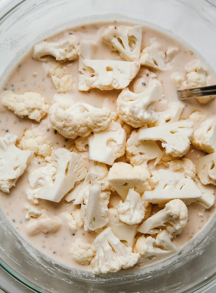 Image shows a bunch of cauliflower florets in a bowl with a beige batter.