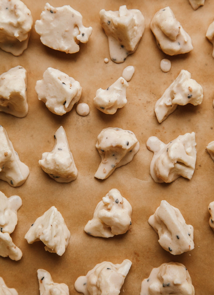Image shows cauliflower florets coated in batter on a parchment-lined baking sheet.
