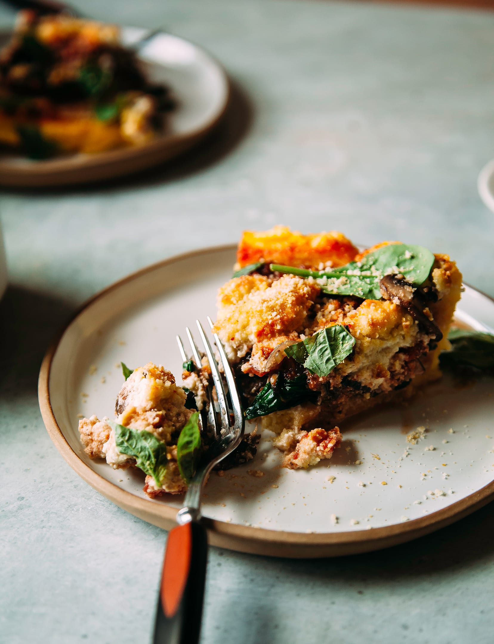 A 3/4 angle of a slice of spinach and mushroom polenta pie on a plate with a fork.