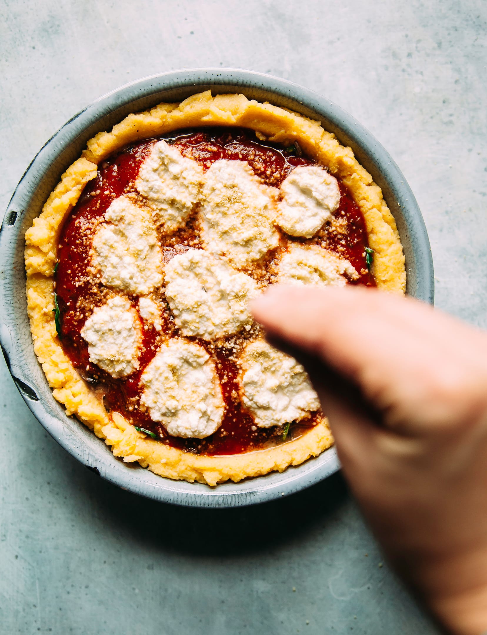 Image shows a hand sprinkling a vegan “Parmesan” over a filled polenta pie.