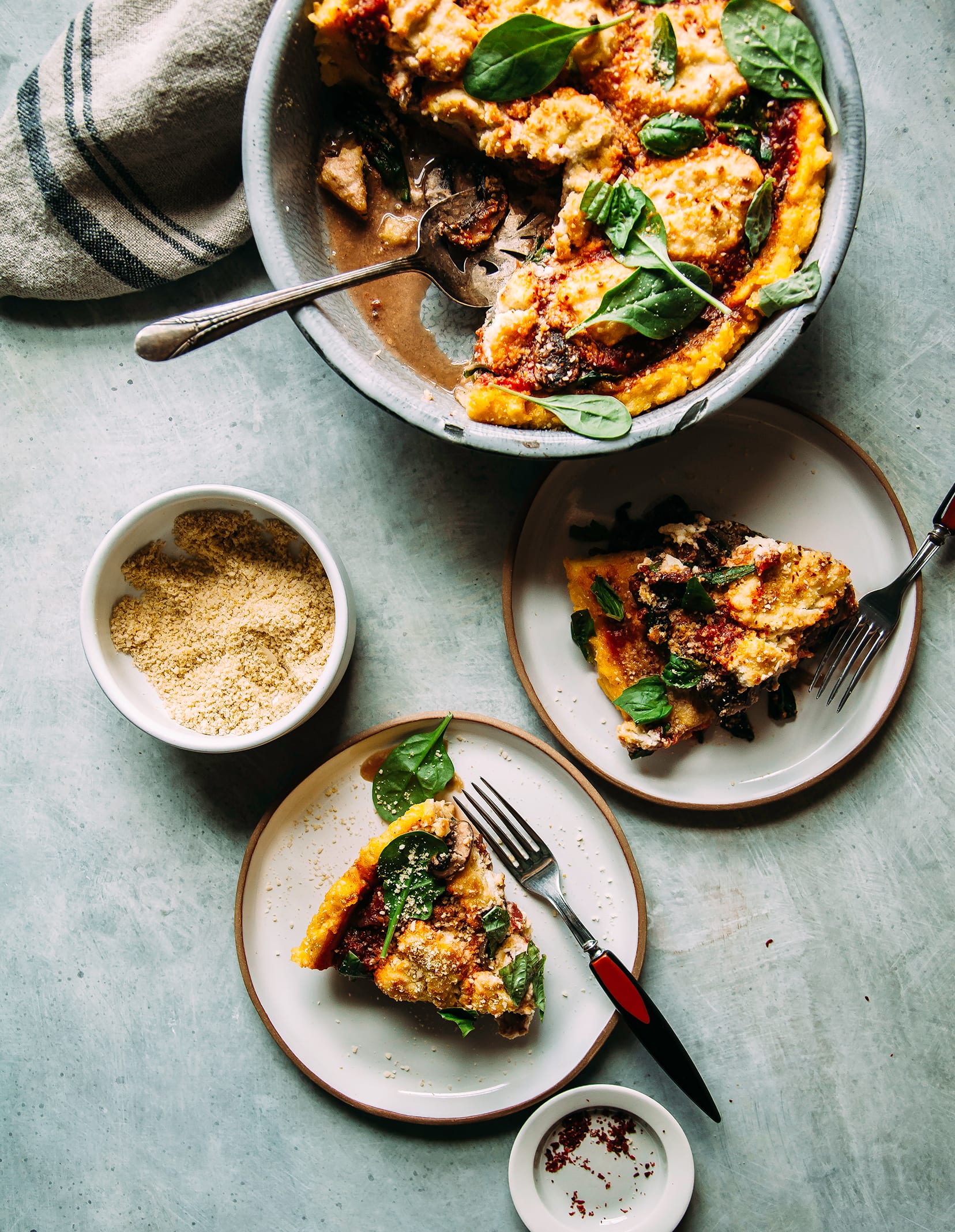 Image shows a baked polenta pie with a deep red tomato and dairy-free ricotta filling. Slices are on individual plates to the side.
