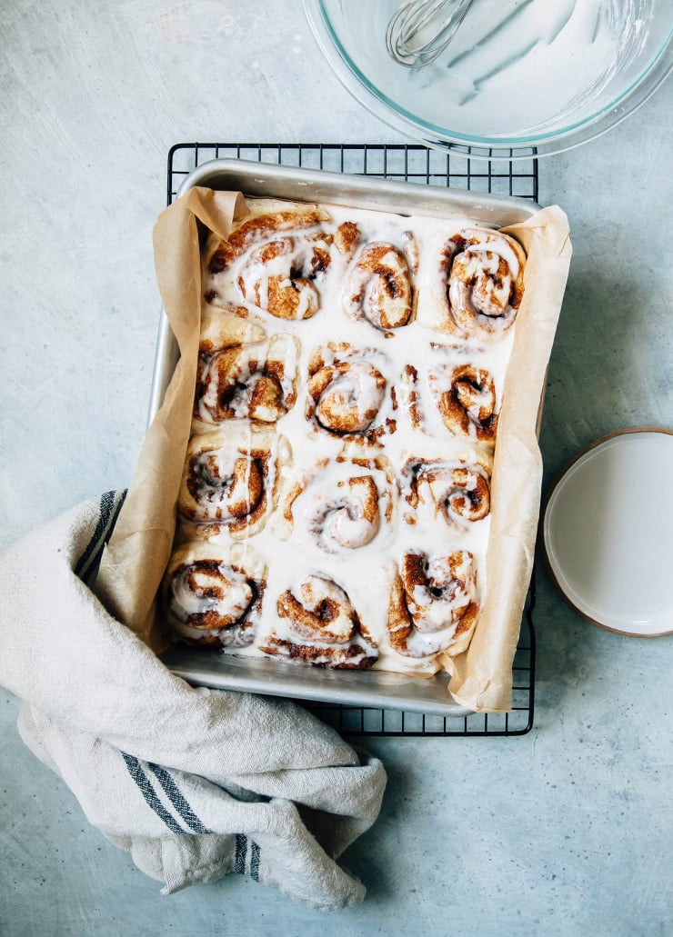An overhead shot of a pan of vegan cinnamon rolls with icing on top. The pan is on top of a cooling rack.