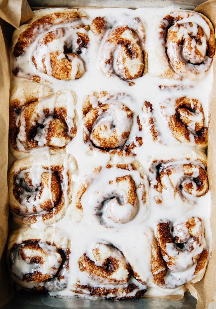 An overhead shot of vegan cinnamon rolls in a pan. The rolls are covered in a white icing. Part of a roundup of vegan holiday recipes