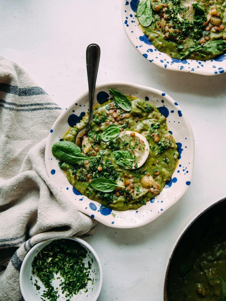 An overhead shot of a deep green lentil stew with spinach and lemon in a blue speckled bowl.