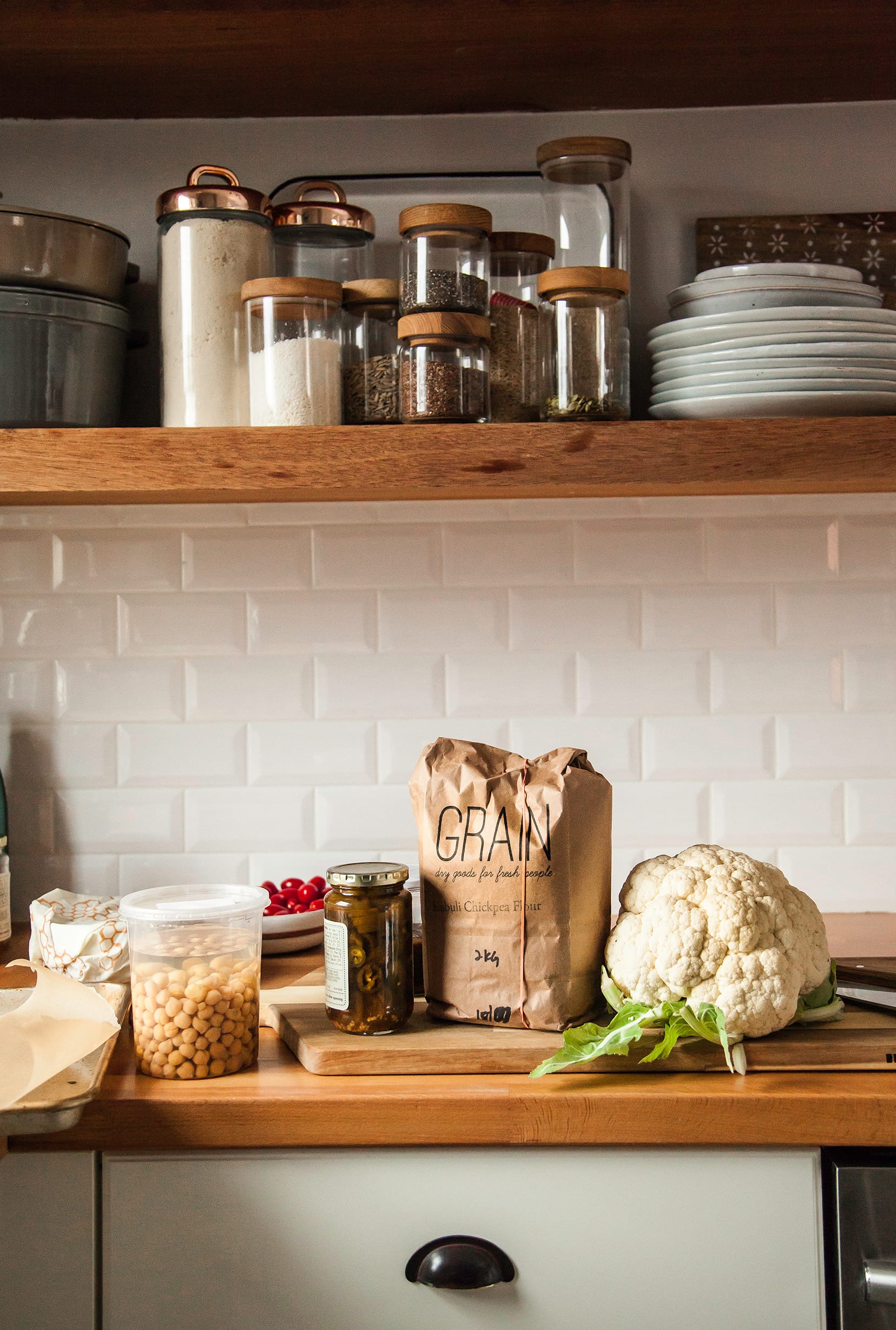 Image shows ingredients for a salad on a butcher block countertop in a white tiled kitchen.