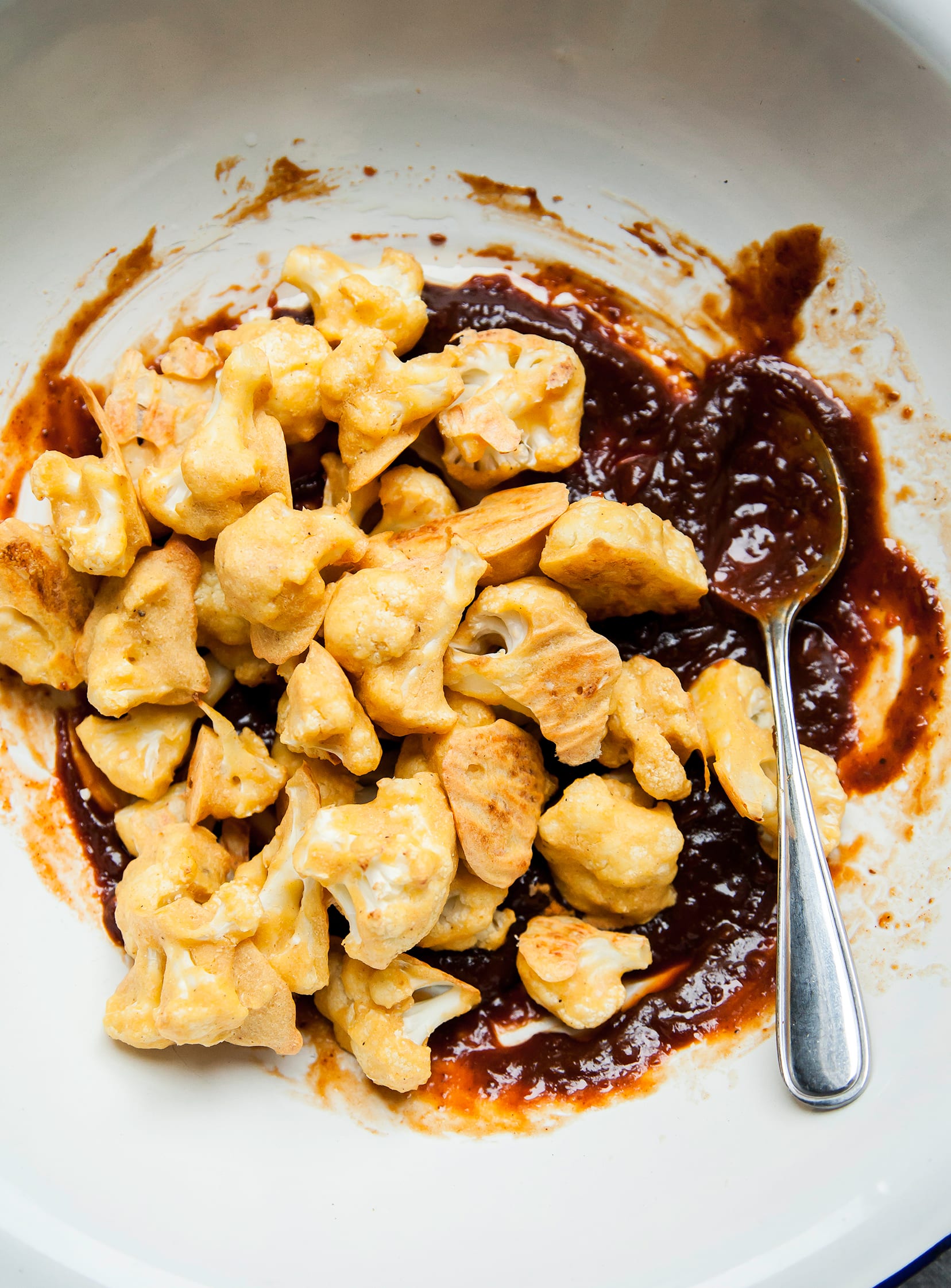 Image shows battered and baked cauliflower being coated with BBQ sauce.