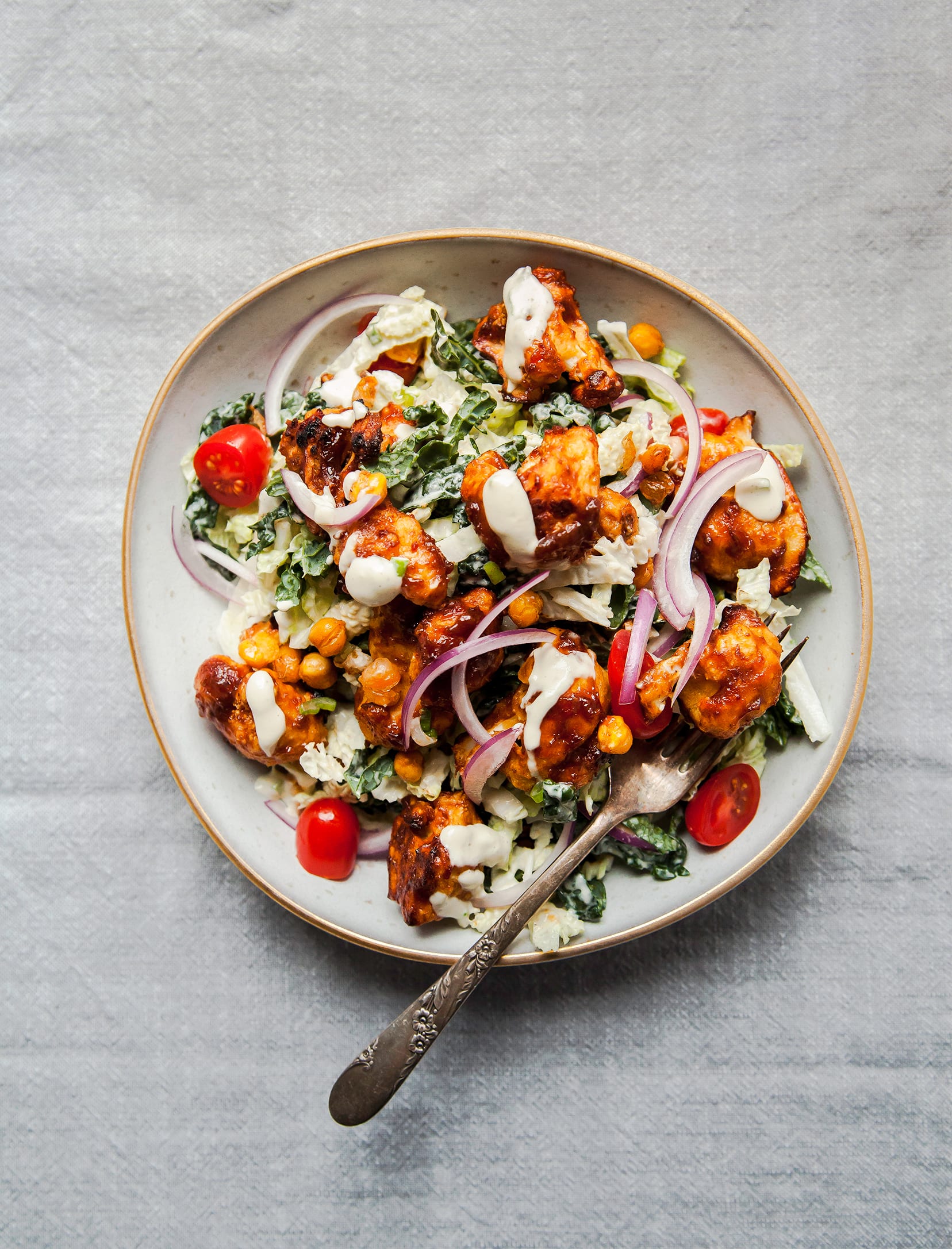 An overhead shot of a Napa cabbage and kale salad topped with BBQ cauliflower, chickpeas, and creamy dressing.