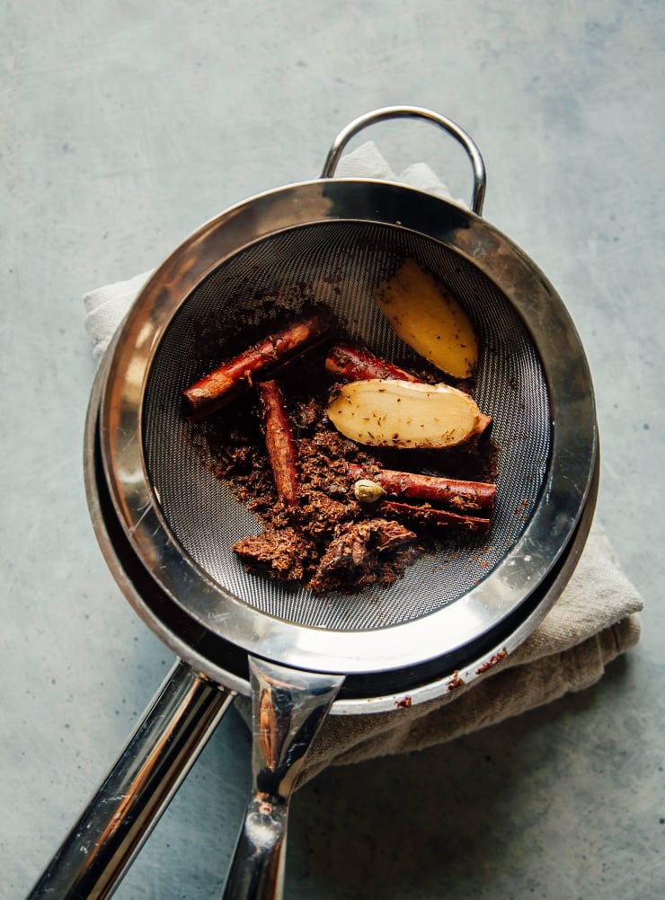 Rooibos tea and masala chai spices being strained in a fine mesh strainer to make a concentrate.