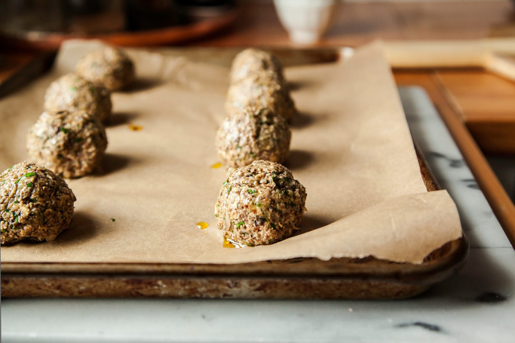 Image shows rolled up vegan meatballs on a baking sheet, before baking.