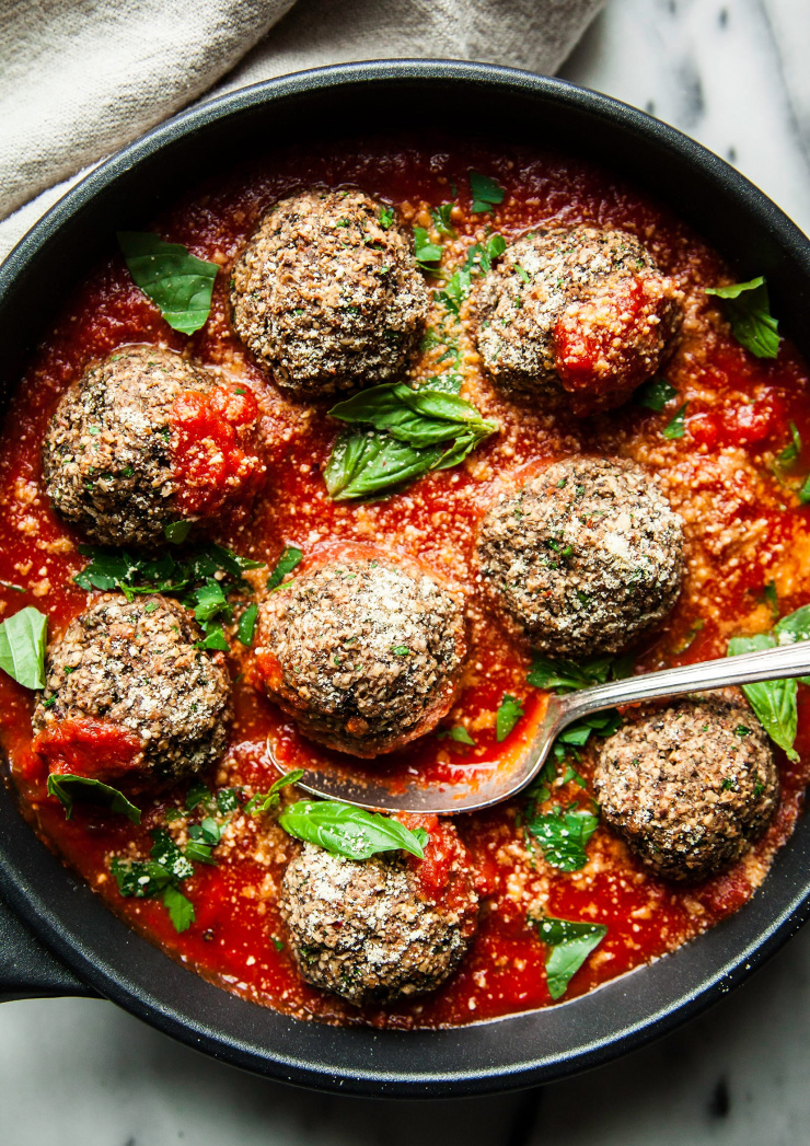An up close overhead shot of vegan meatballs in a skillet, covered in marinara sauce and garnished with fresh basil.