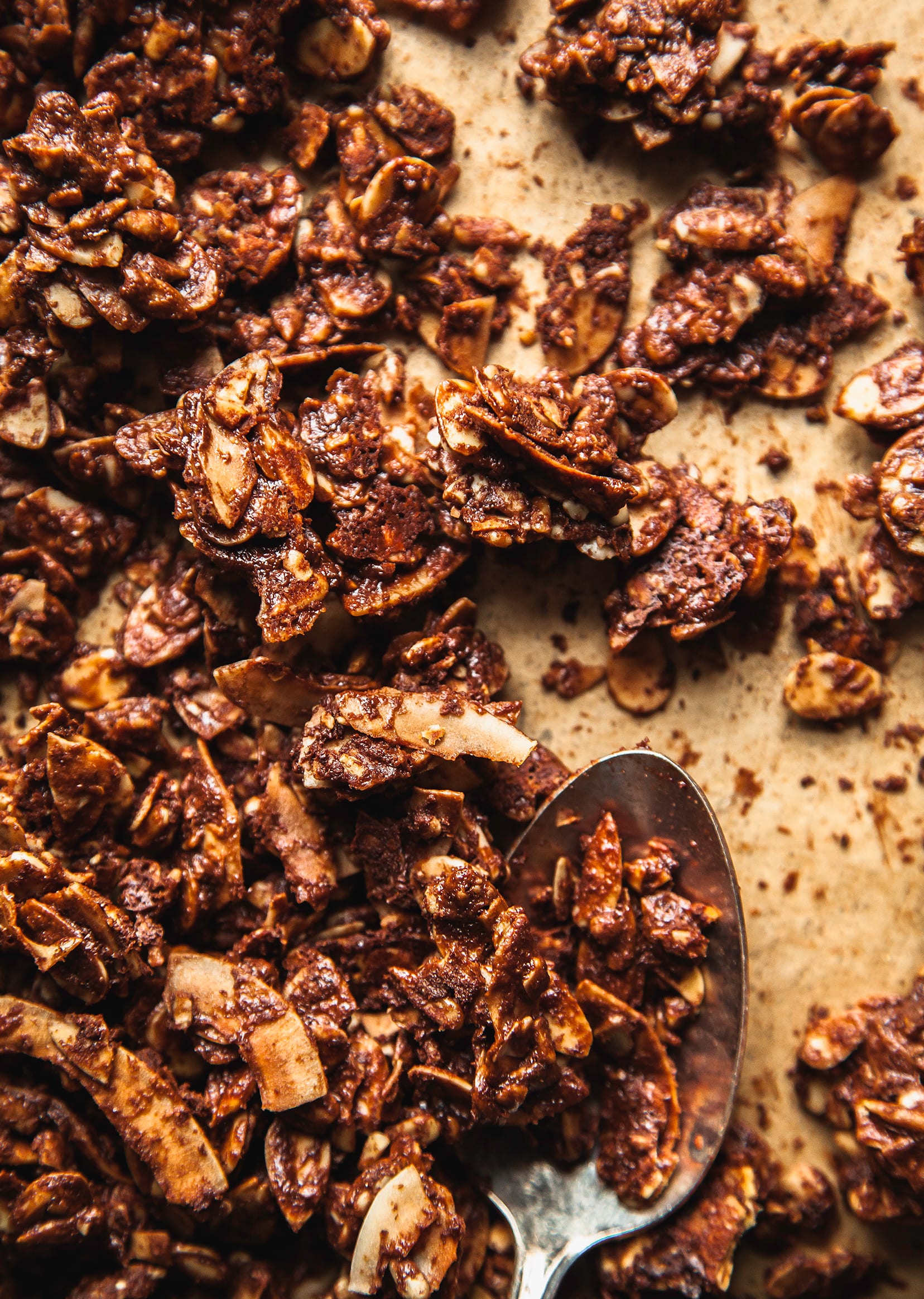 An overhead shot of deep brown, chocolate granola hunks on a parchment lined baking sheet. The image is taken up close.