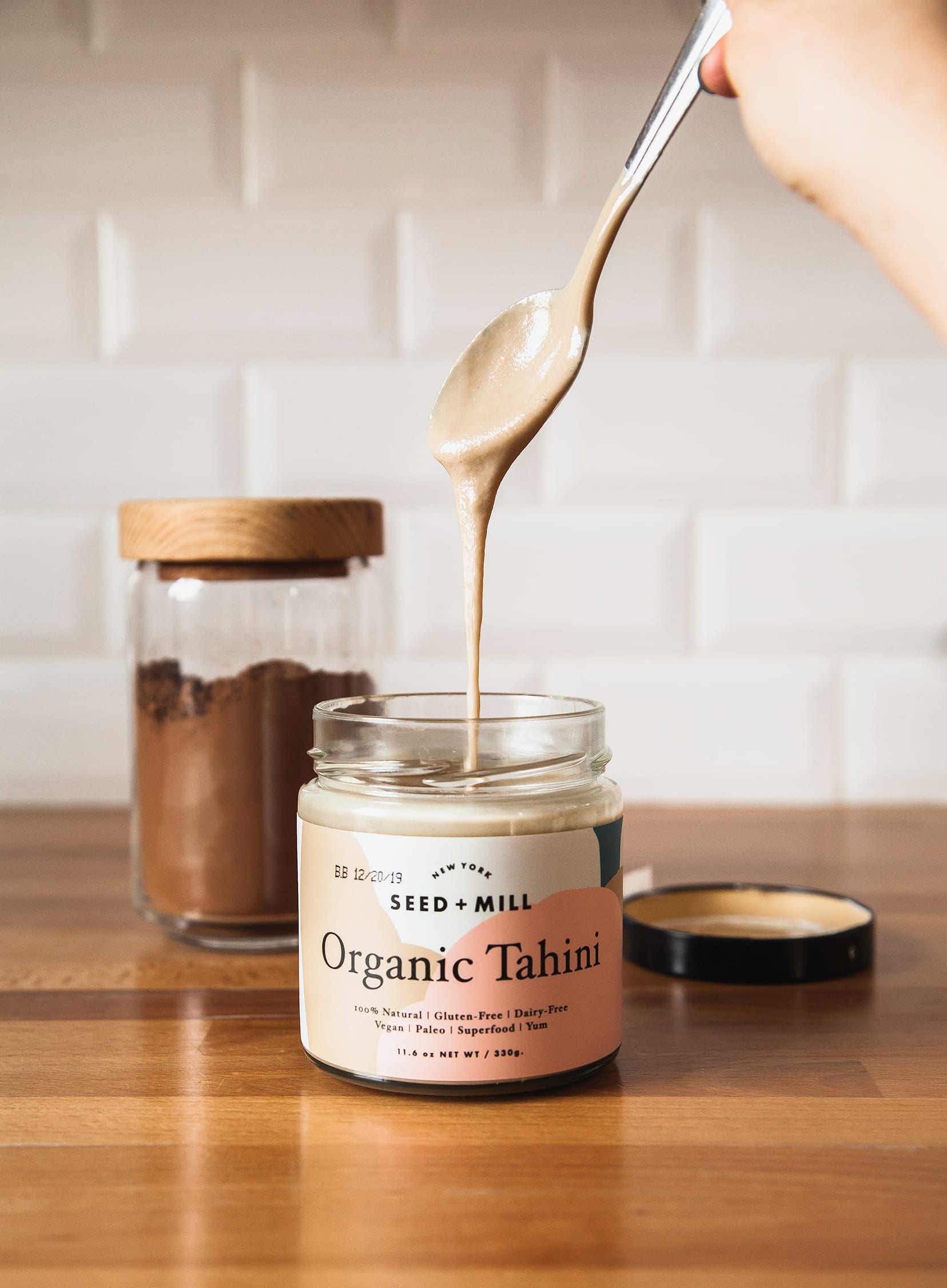 Image shows a spoon lifting out of a jar of tahini with tahini dripping off of the spoon.