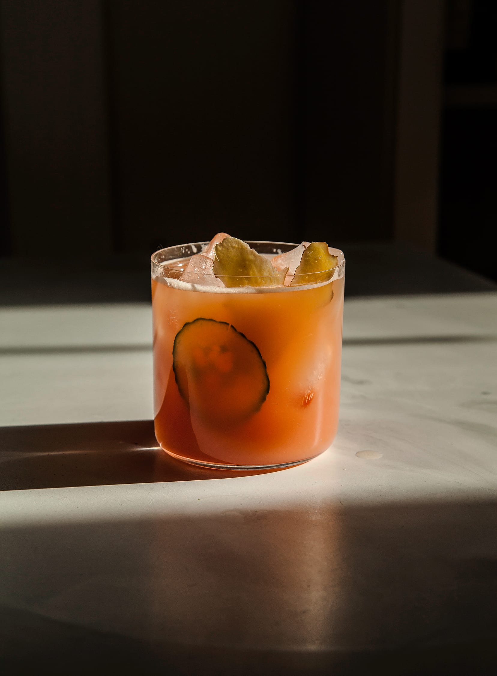 A head on shot of a glass of pink juice, garnished with a cucumber slice and a ginger slice.