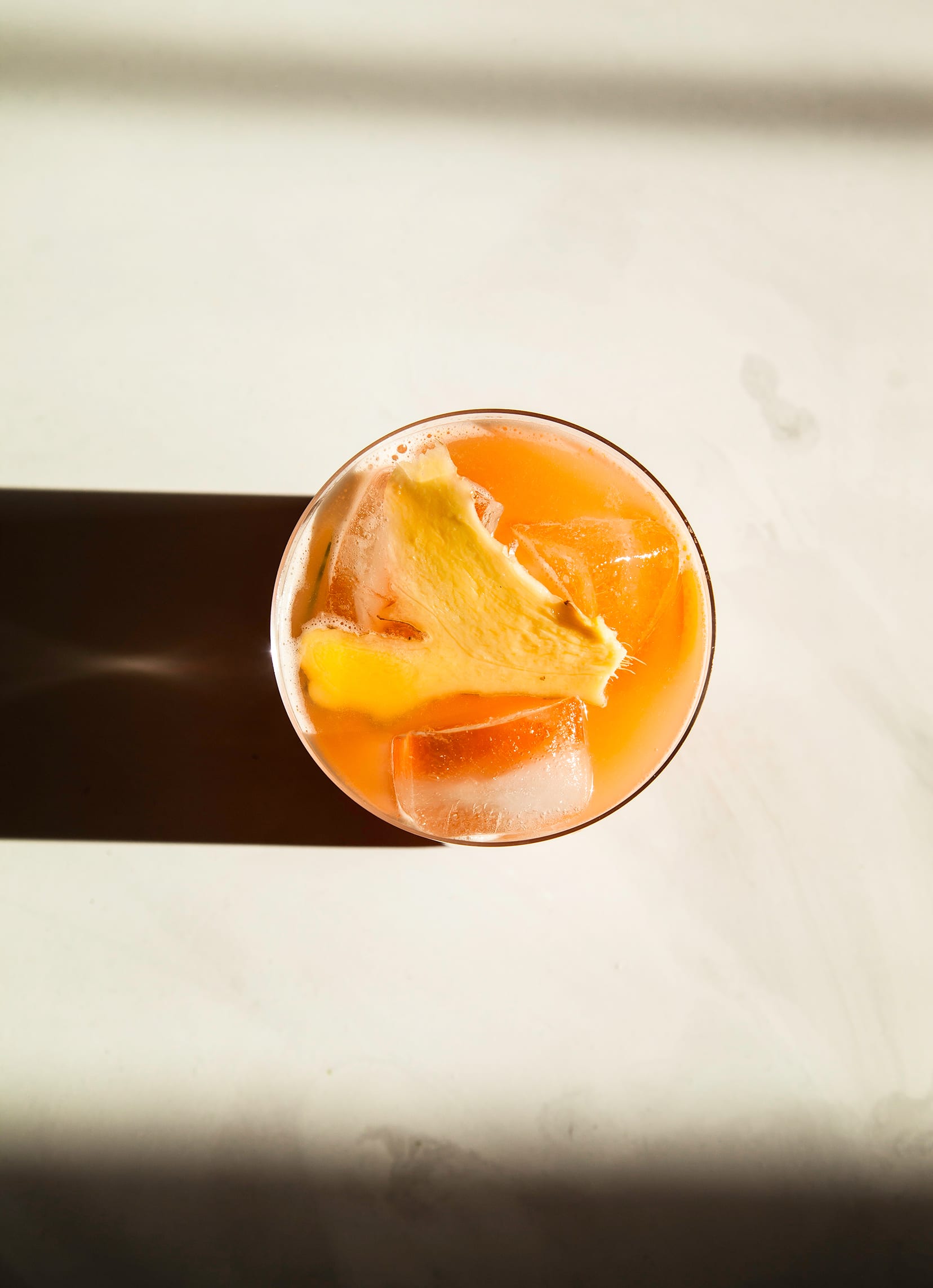An overhead shot of a glass of pink juice with a slice of ginger as a garnish.