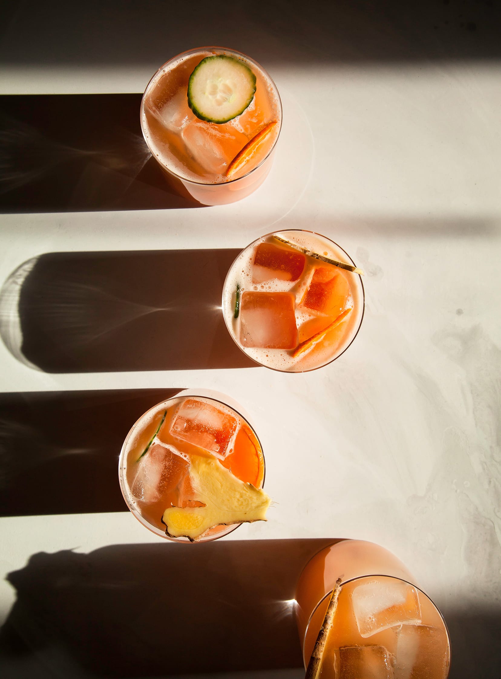 An overhead shot of a pink-hued winter sparkle juice in 4 glasses, taken in direct sunlight.