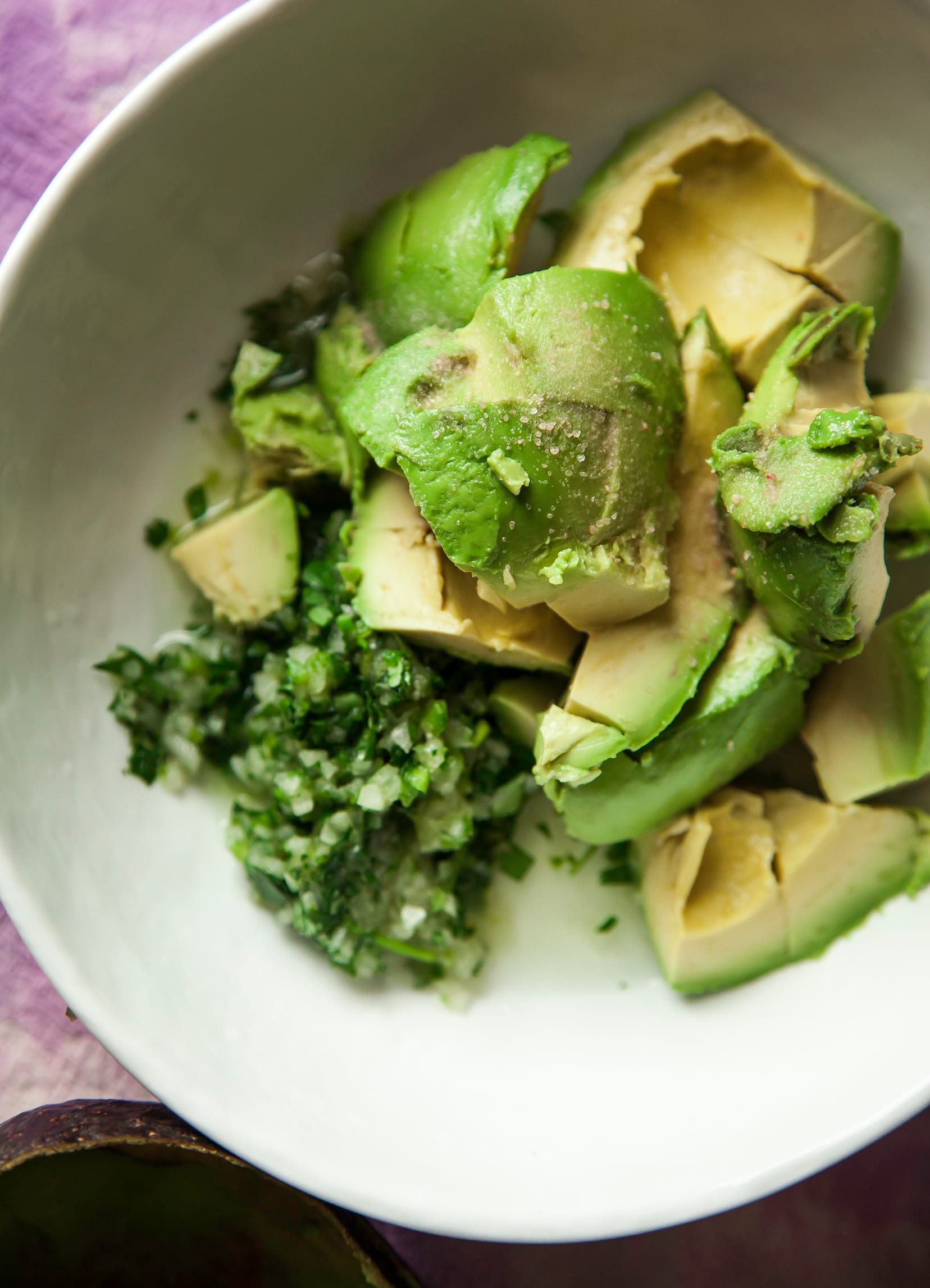 An up close shot of diced avocado, minced onion, jalapeno, and cilantro in a white bowl before being mashed into guacamole.