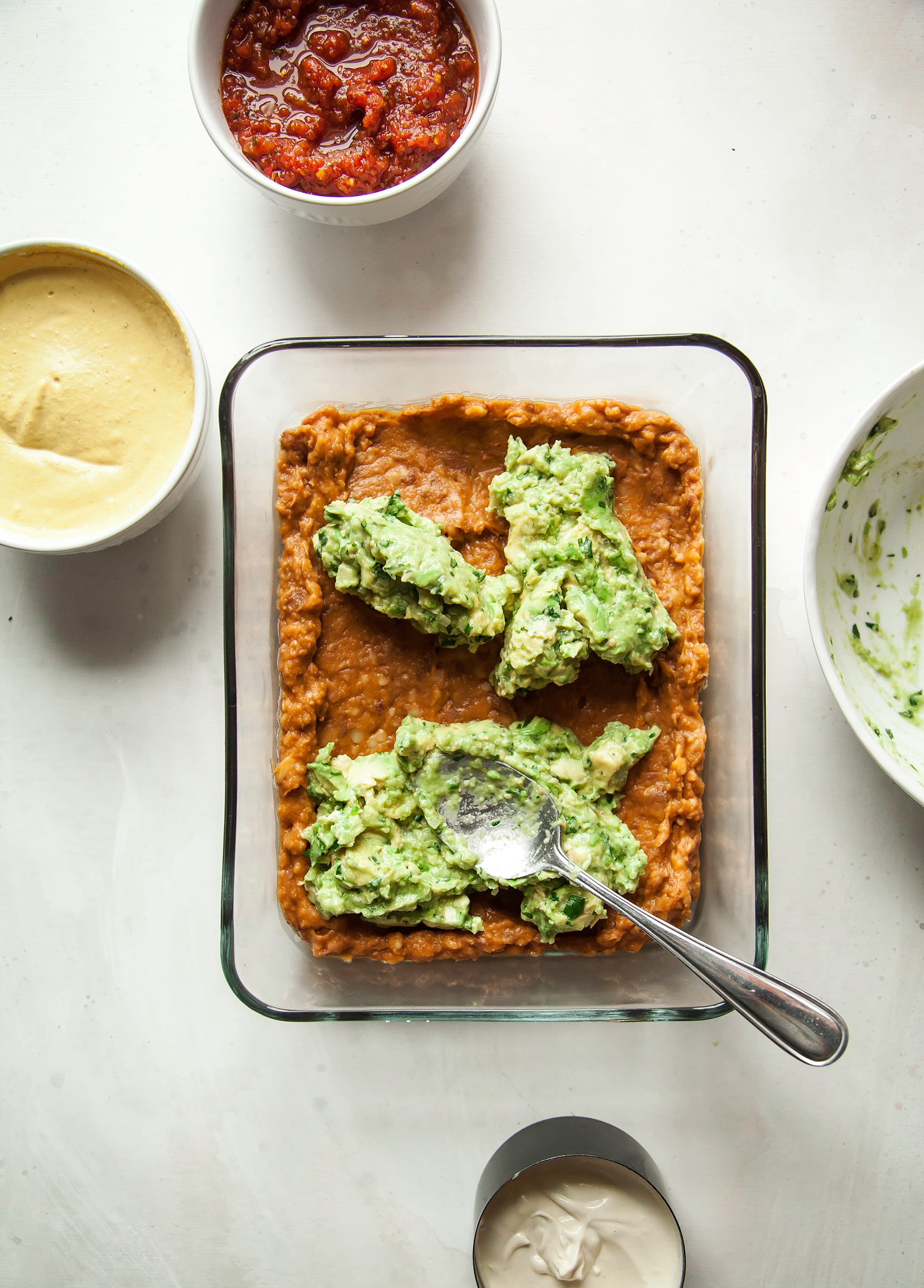 An overhead shot of guacamole being spread on top of retried beans.