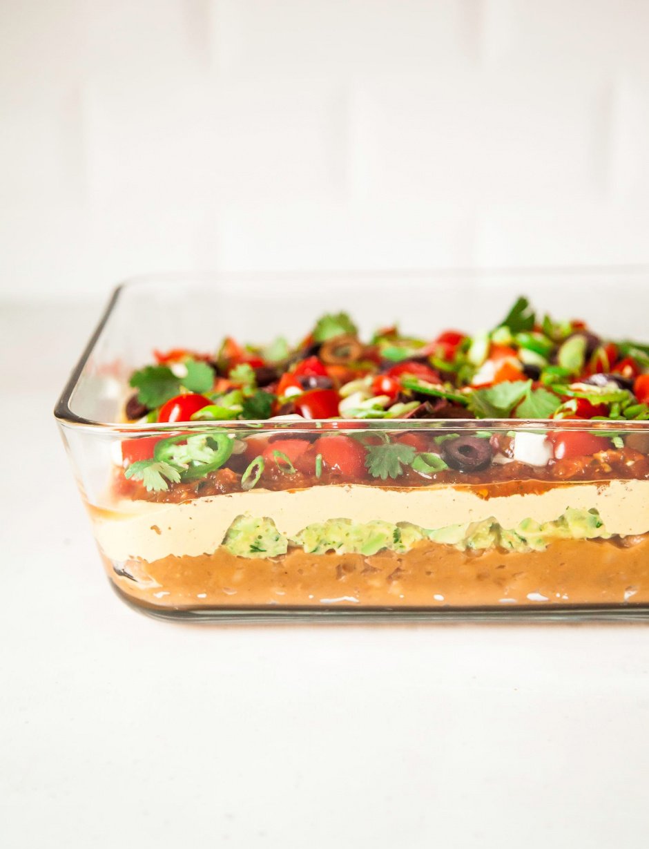 A head on image of a 7-layer dip captured in a glass container against a white background.