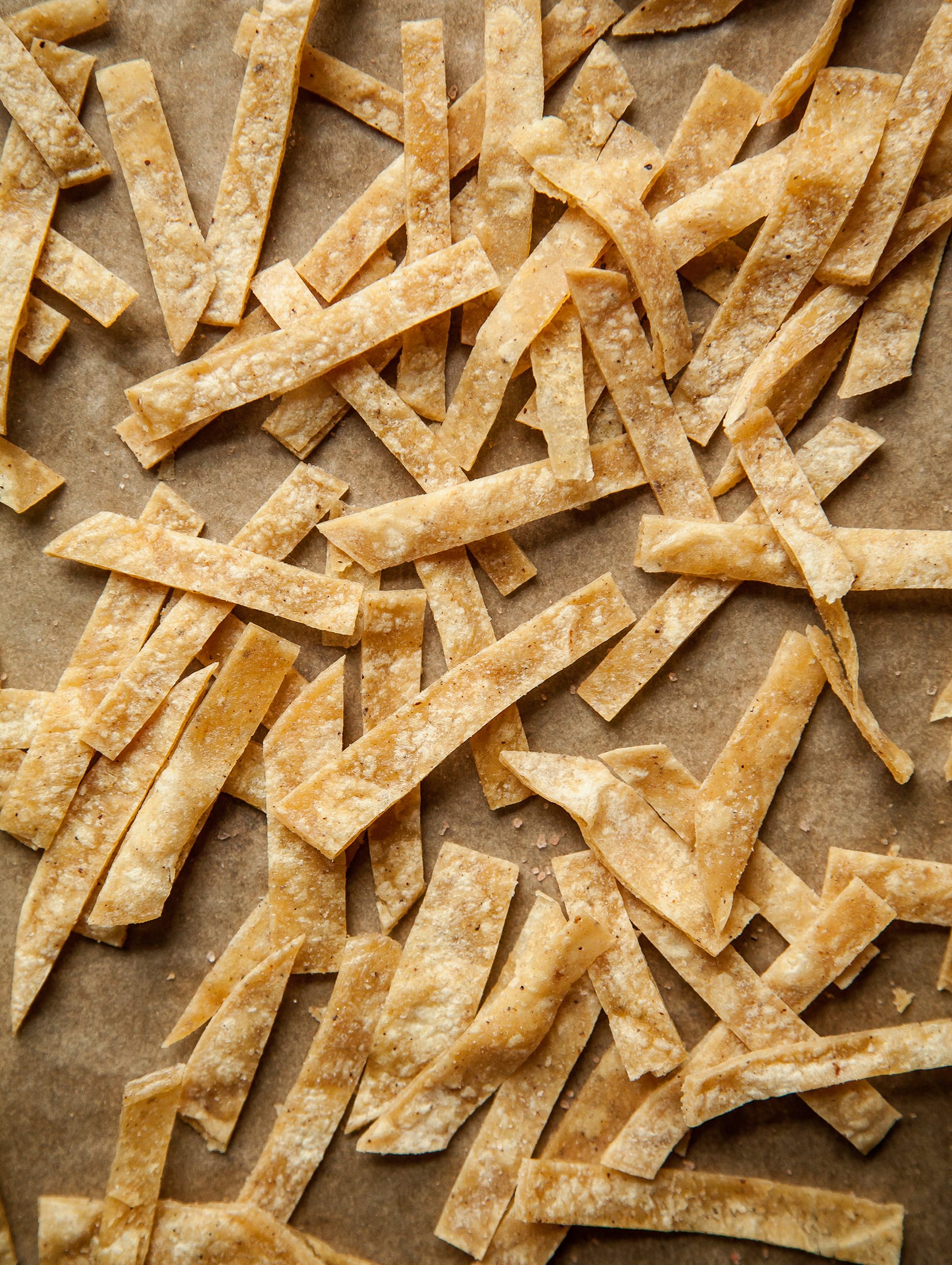 An overhead, up close shot of crispy corn tortilla strips on a parchment lined baking sheet.