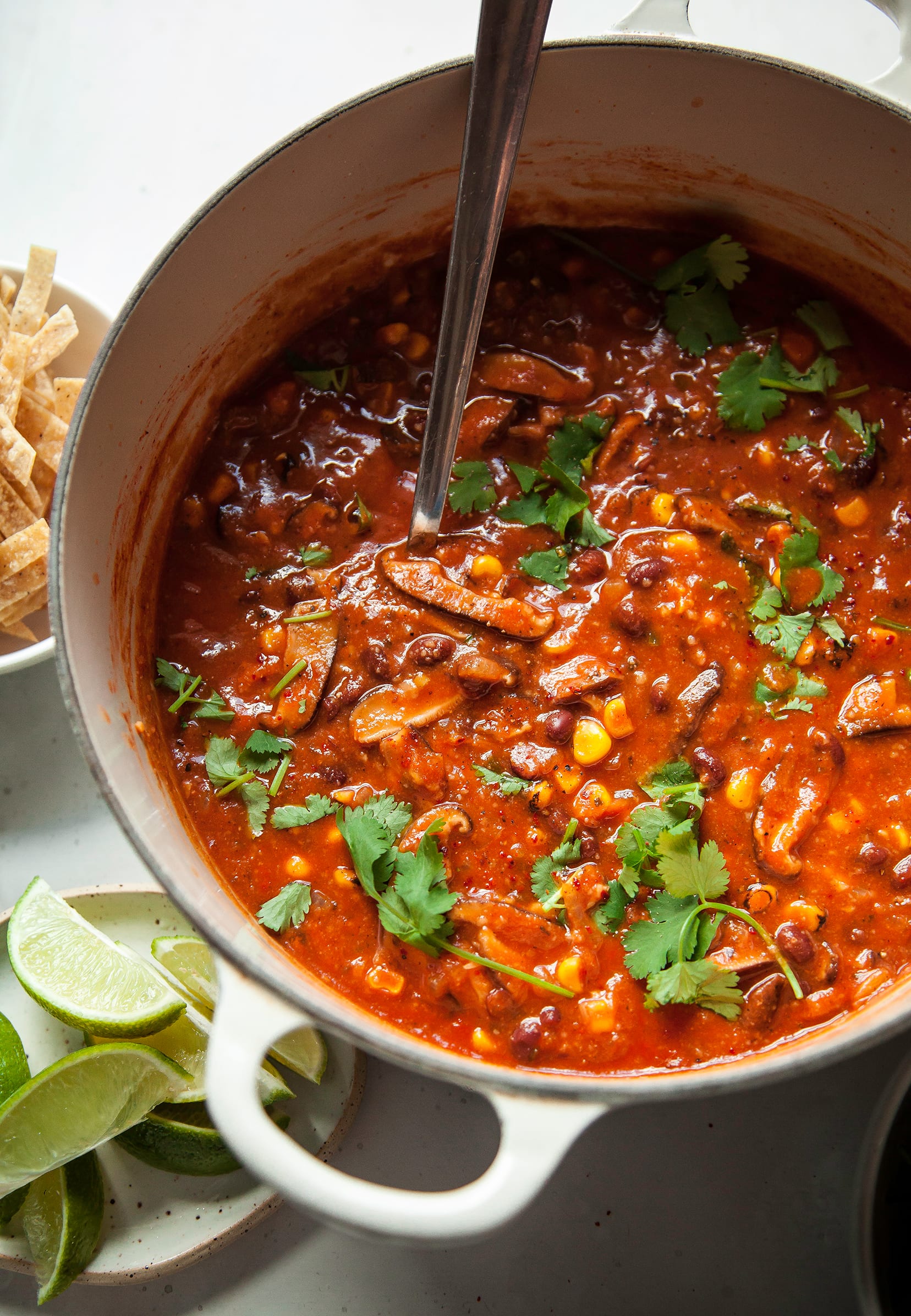 An overhead shot of smoky shiitake tortilla soup in a beige Dutch oven.