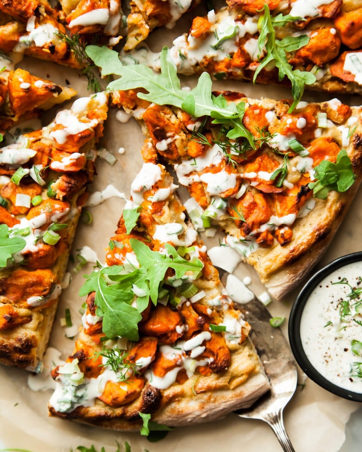 An overhead shot of a sliced vegan buffalo cauliflower pizza, drizzled with a creamy white sauce.