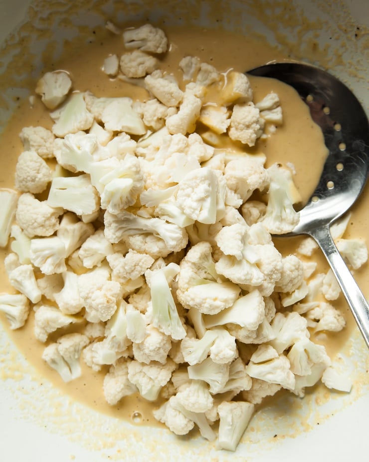 Image shows chopped cauliflower about to be tossed with a beige batter.
