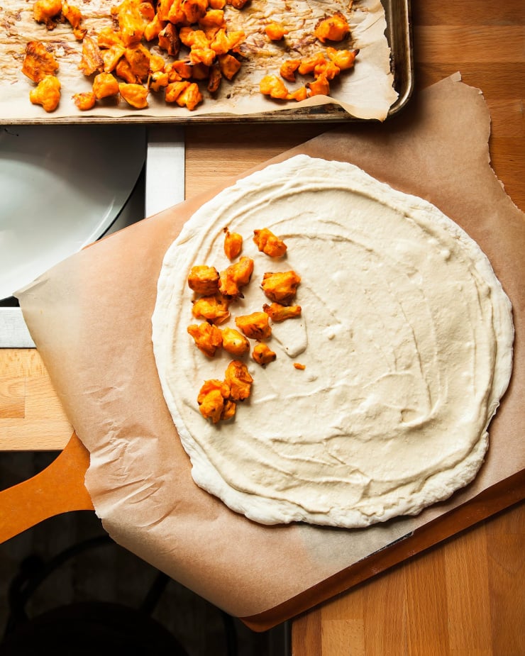 Image shows a Buffalo cauliflower pizza in the early stages of being assembled.