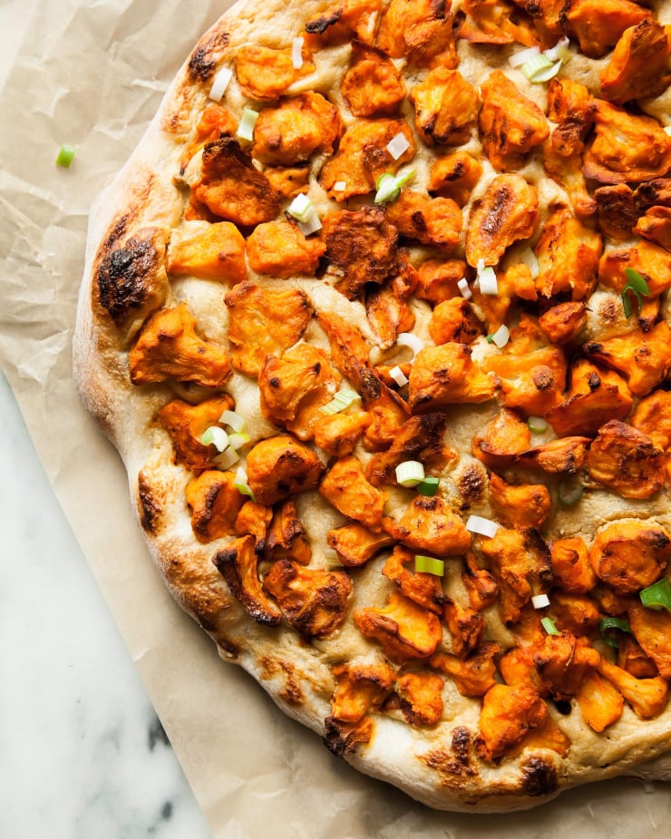 Image shows a baked pizza with Buffalo cauliflower on top.