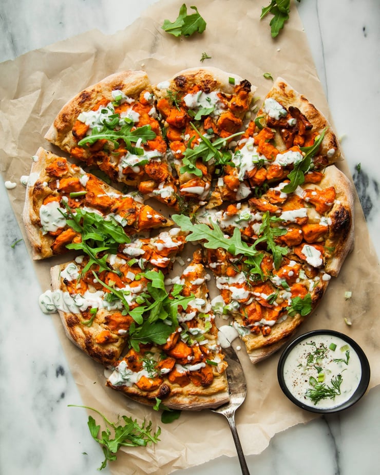 An overhead shot of a sliced vegan buffalo cauliflower pizza, drizzled with a creamy white sauce.