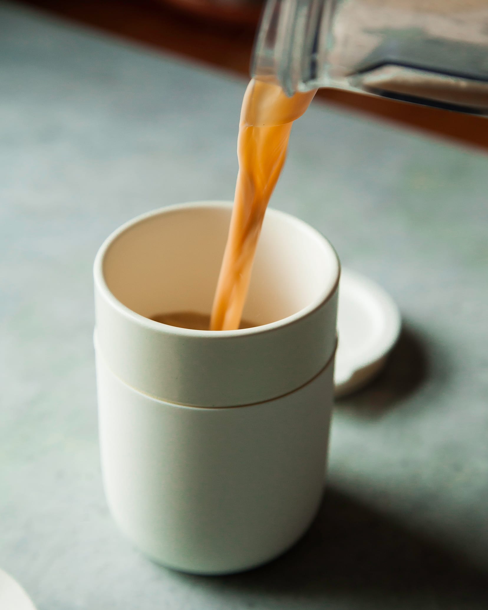 A tea latte is being poured into a white to-go mug.